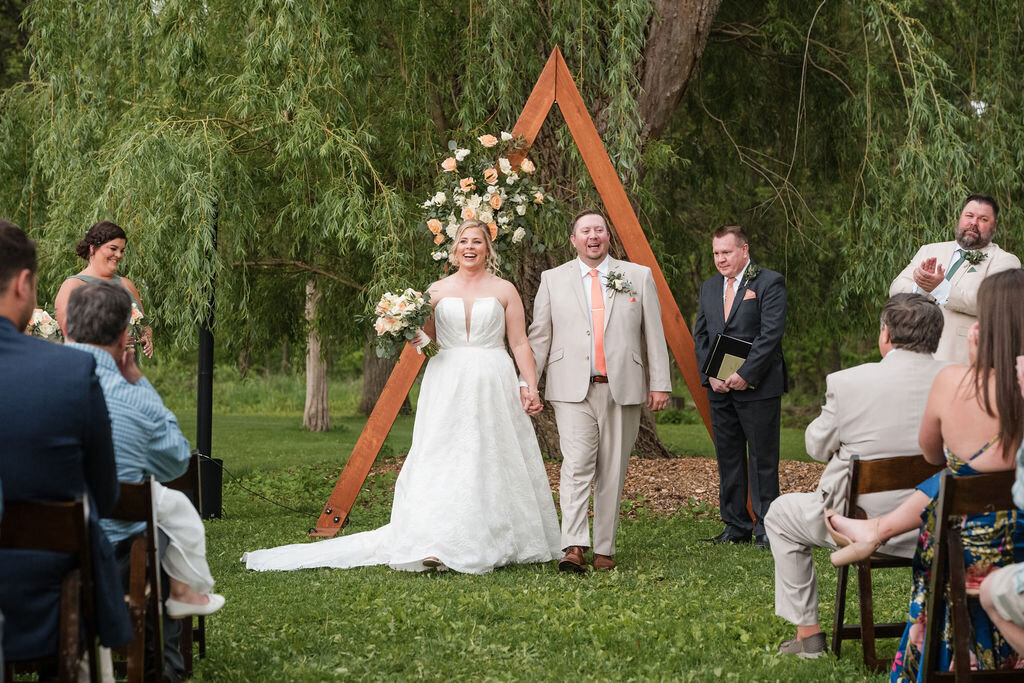 bride and groom holding hands at the outdoor wedding ceremony at barnwood events in madison, winconsin.