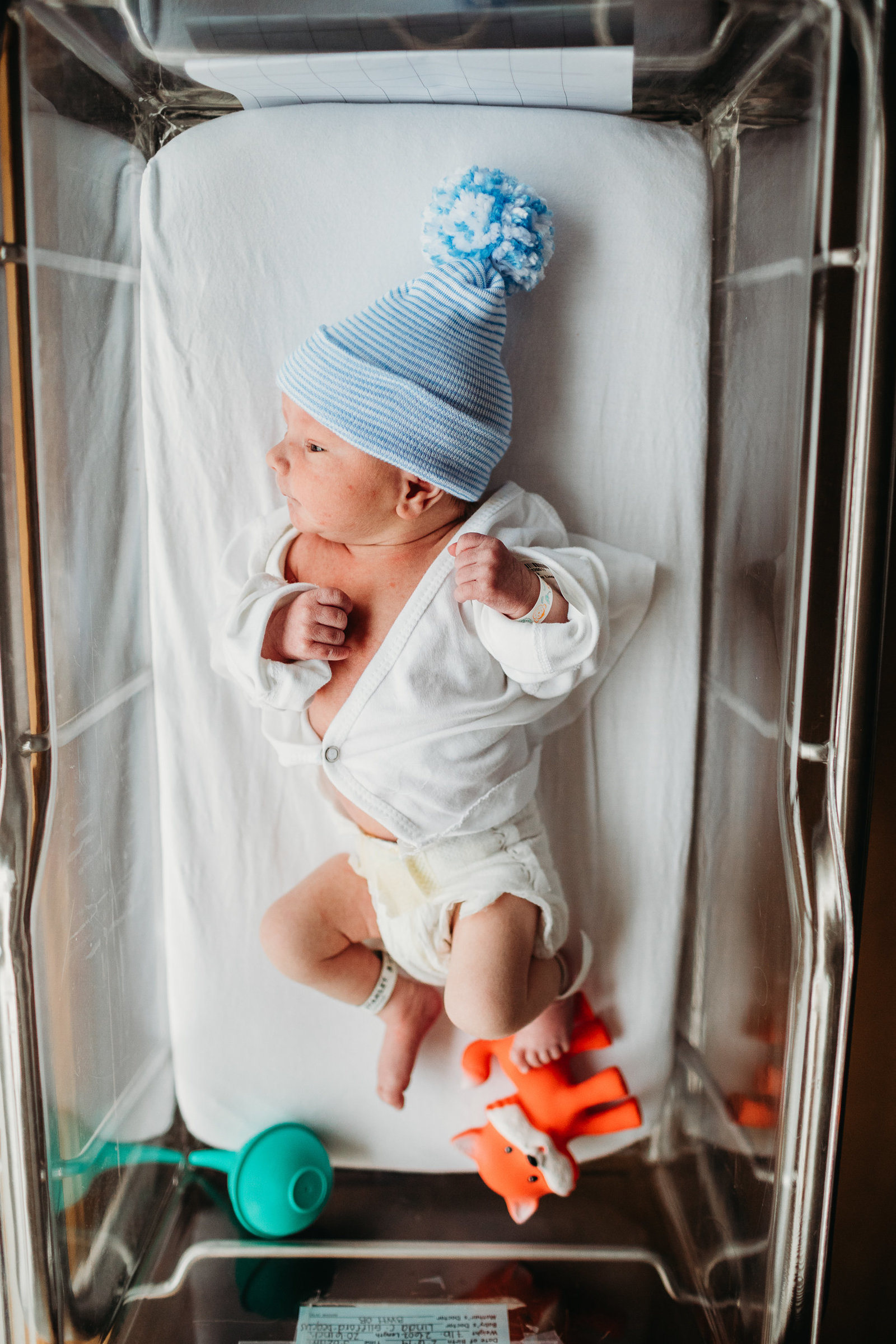 baby with blue hat lies in hospital bassinet