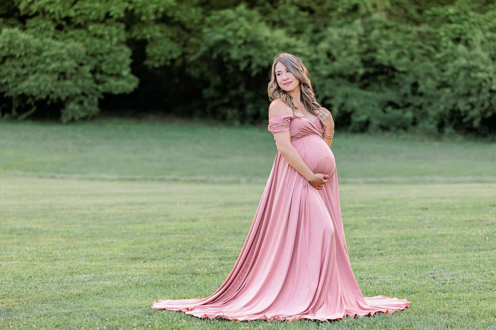A beautiful pregnant woman in pink posing in a field in Burke, VA.