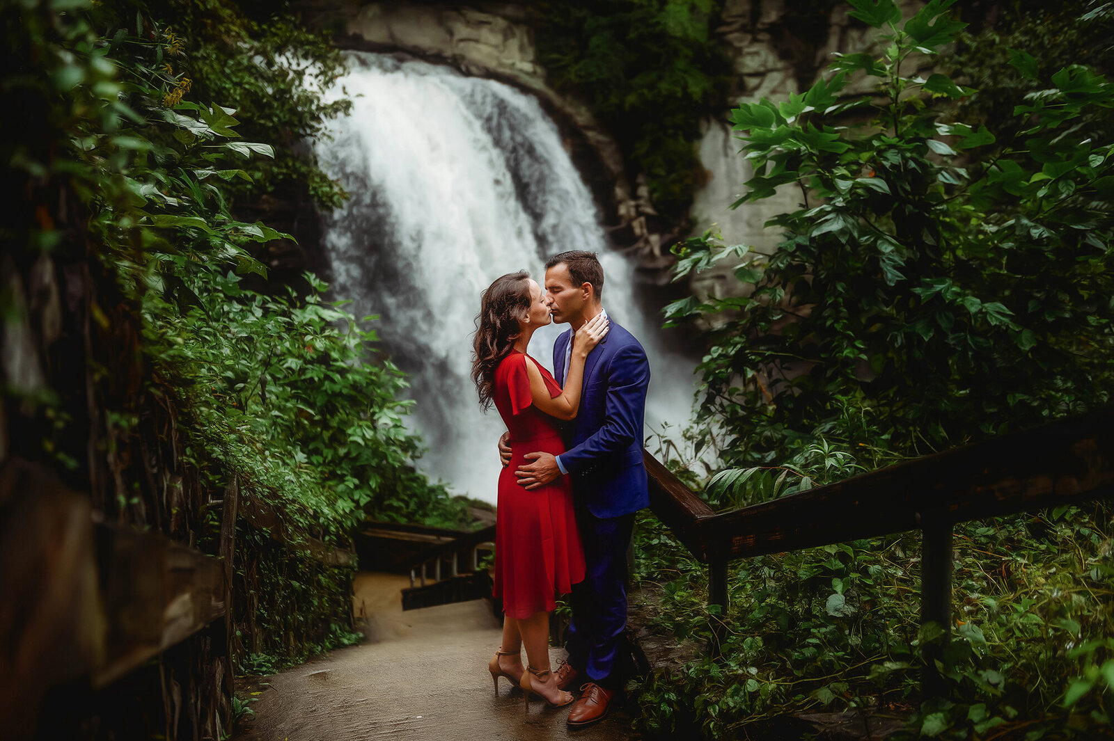 Couple kisses in front of Looking Glass Falls while posing for Engagement Photos near Asheville, NC.