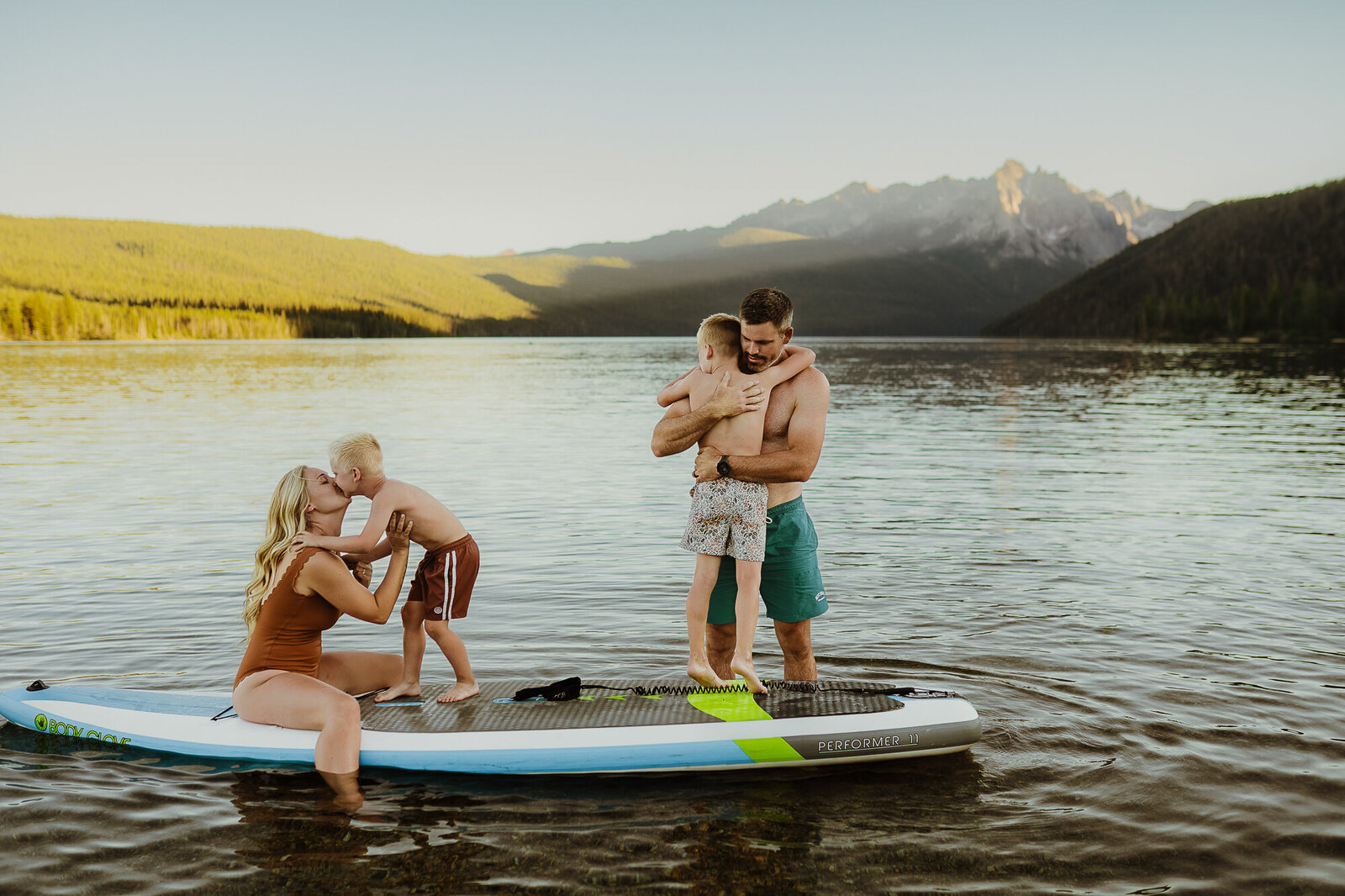 Family of four standing on a paddle board on a lake with the mountains in the background