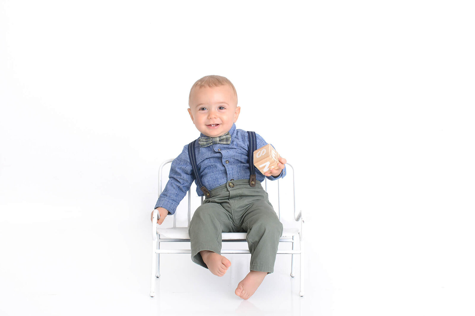 one year old boy sits in a white chair in front of a white background