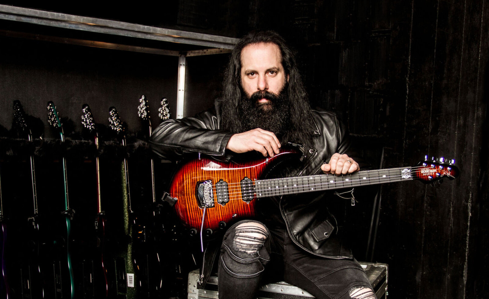 Music  portrait John Petrucci sitting with red guitar wearing black leather jacket
