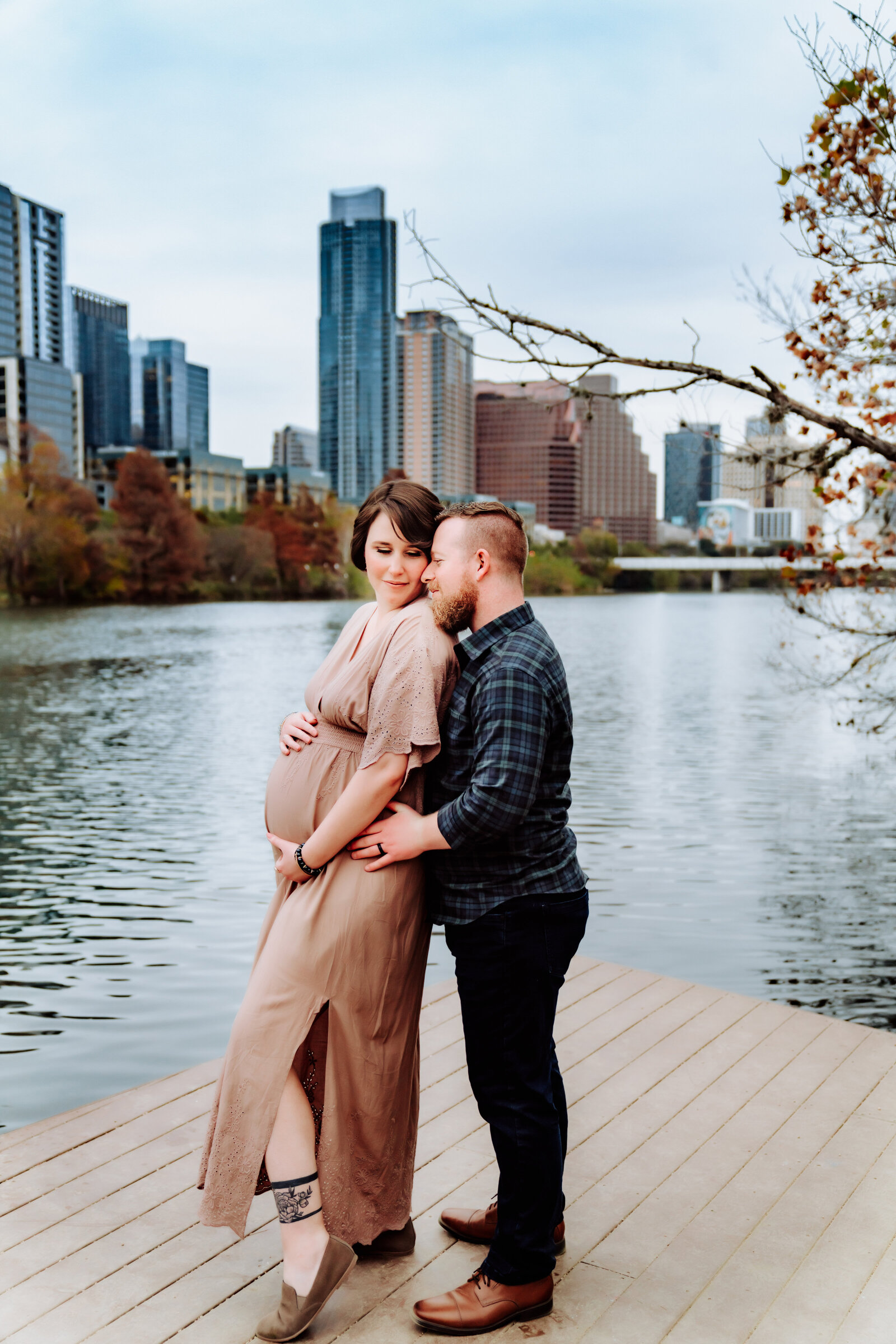 Maternity Photographer, a husband embraces his wife near the river in the city