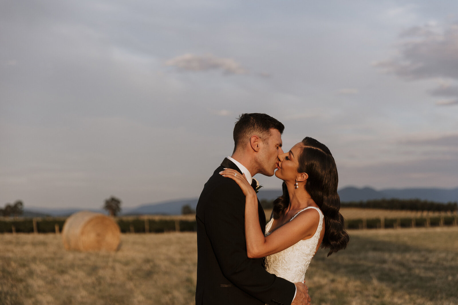 A couple kissing at their Zonzo estate wedding with a hay bail in the background