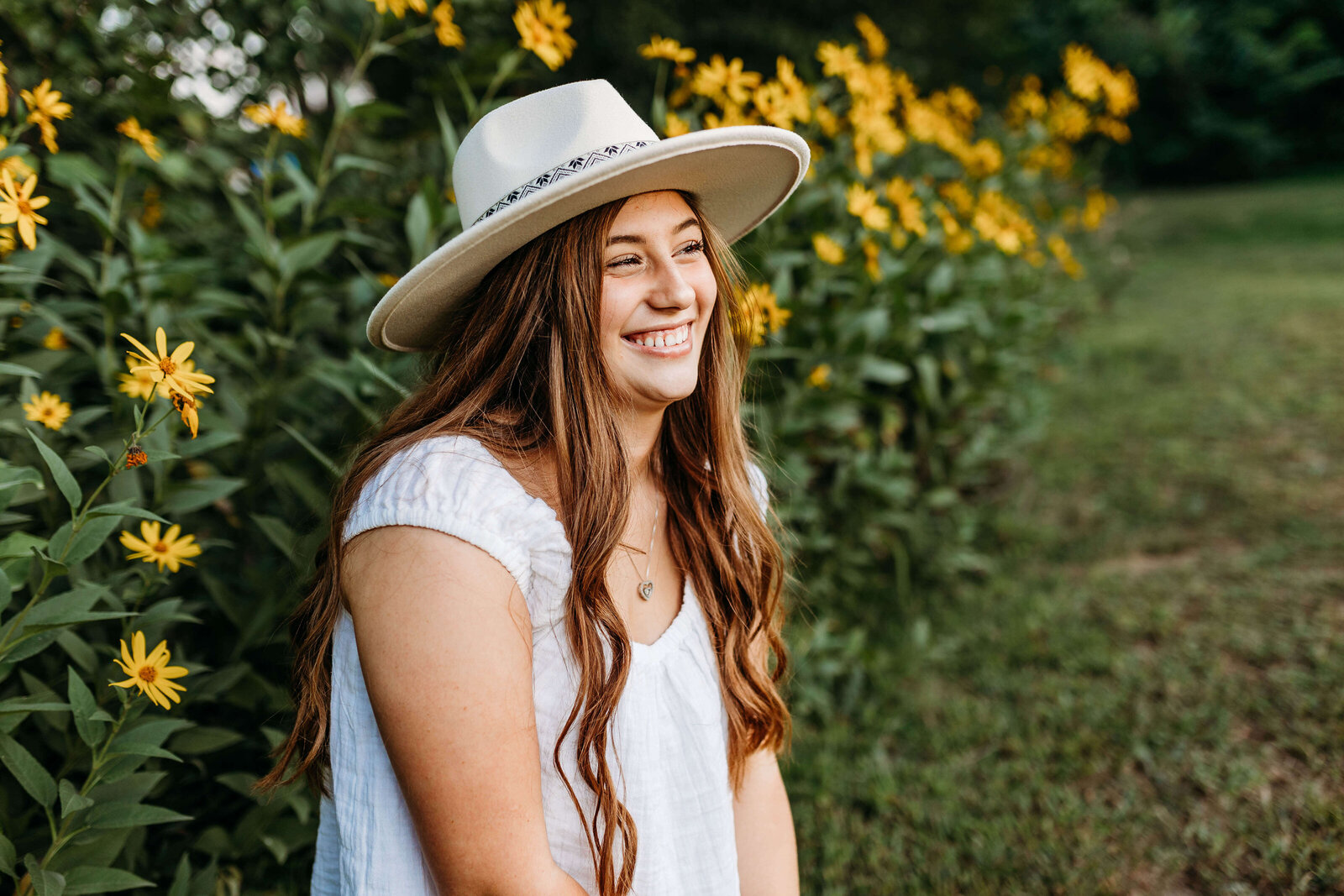 Senior girl smiling while squatting in front of the yellow flowers