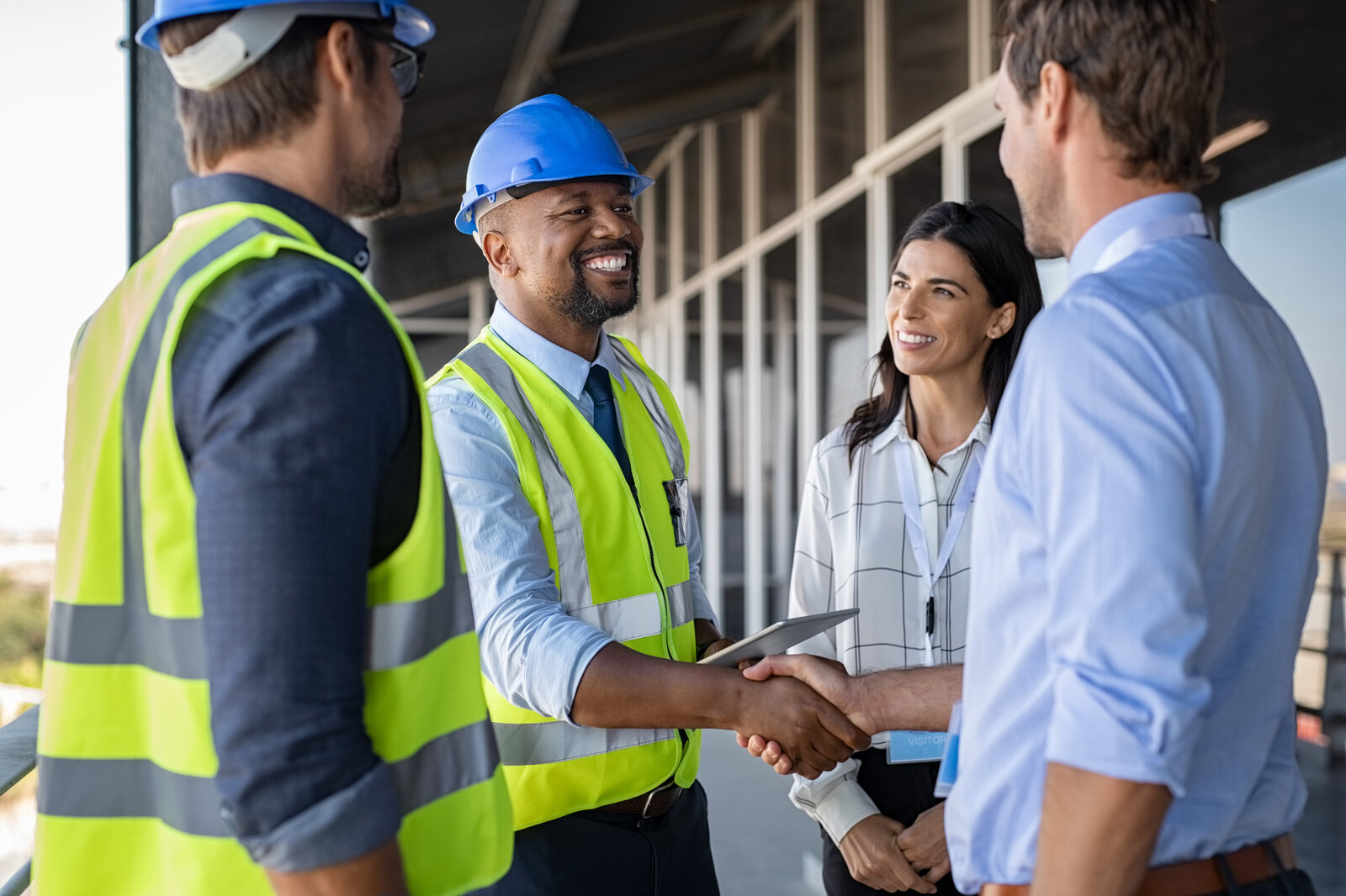 2 men shake hands at a construction site as woman smiles and looks on