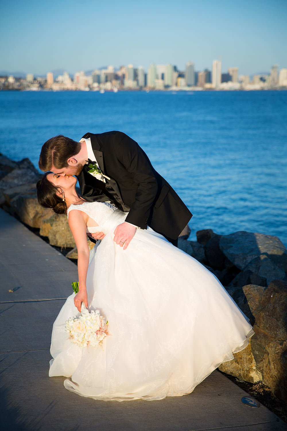 bride and groom kissing with san diego skyline