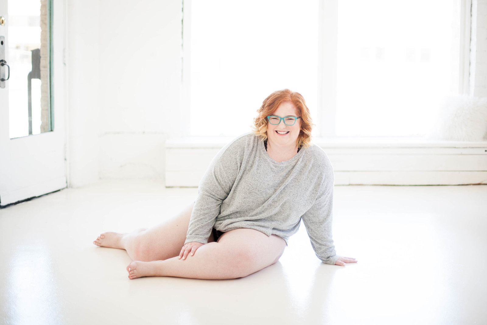 A woman wearing a grey sweater in a white room.