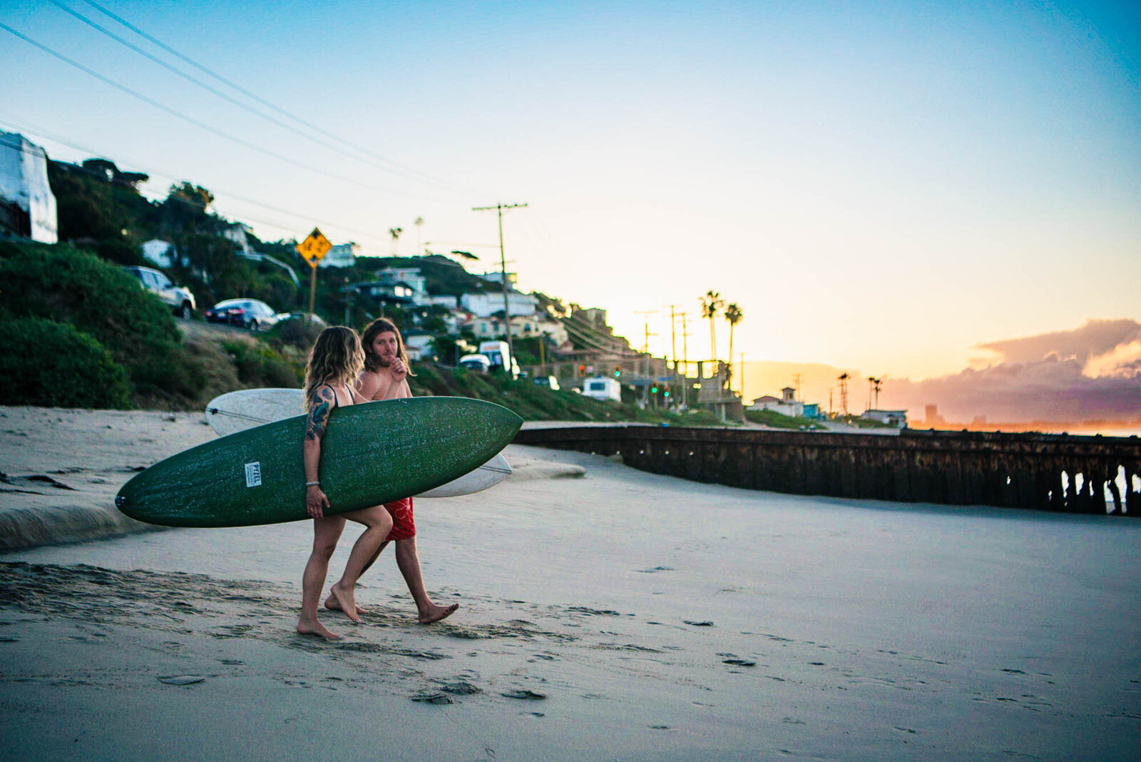 Couple carrying surfboards walks on Los Angeles beach