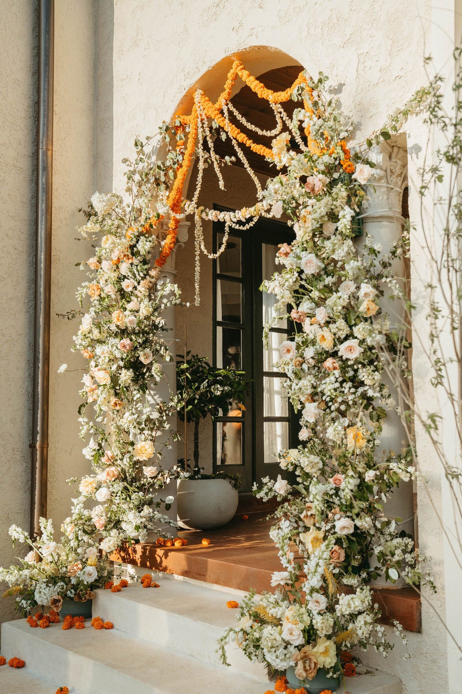 A large floral installation featuring white and orange in an archway with stairs,