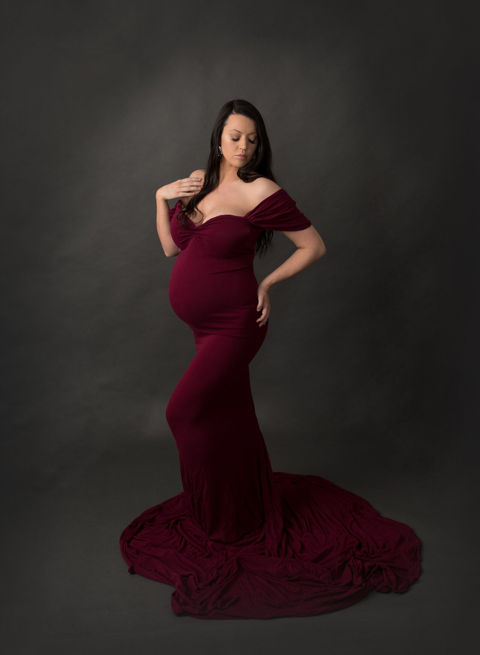 maternty photograph of a woman  wearing a wine coloured dress in a photography studio