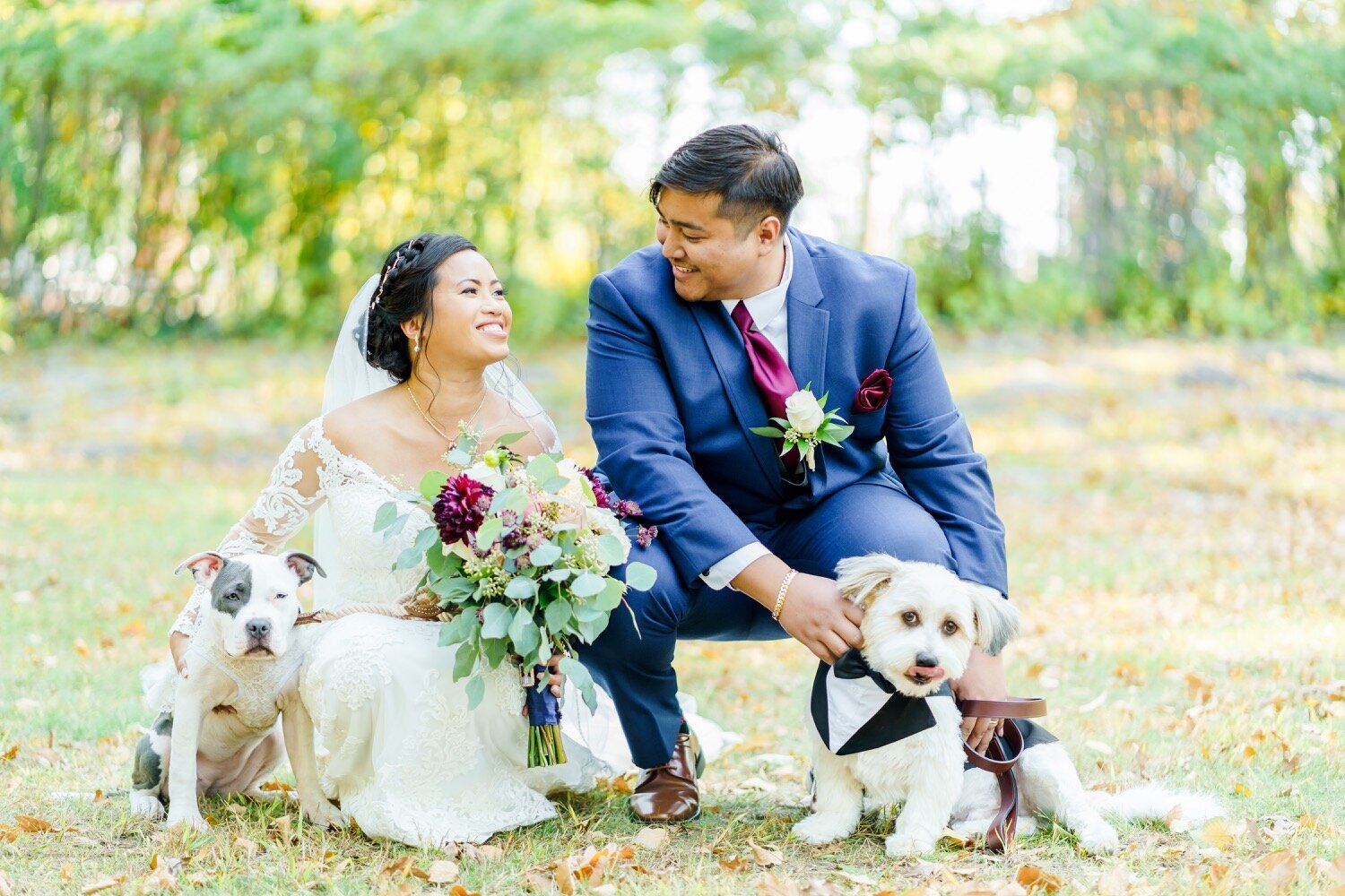 Bride and groom with colorful bouquet bending down and smiling with their dogs