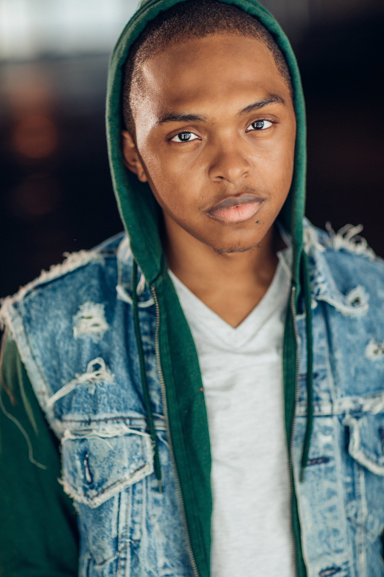 Headshot Photo Of Young Black Man In Blue Denim Vest And Inner Green Hoodie