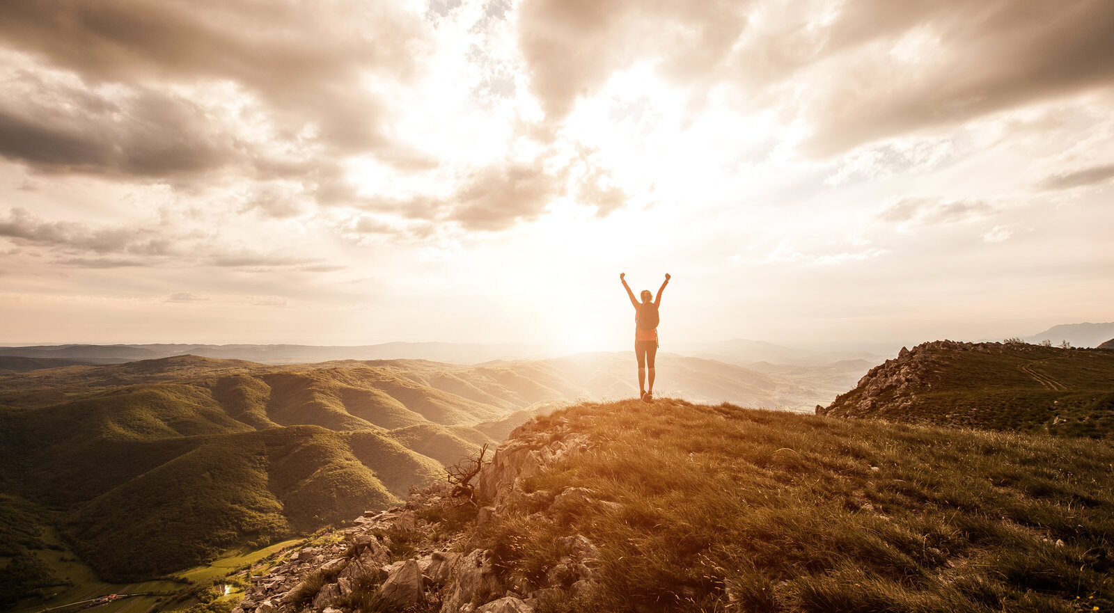 A hiker holds their arms up triumphantly and looks at the sun.