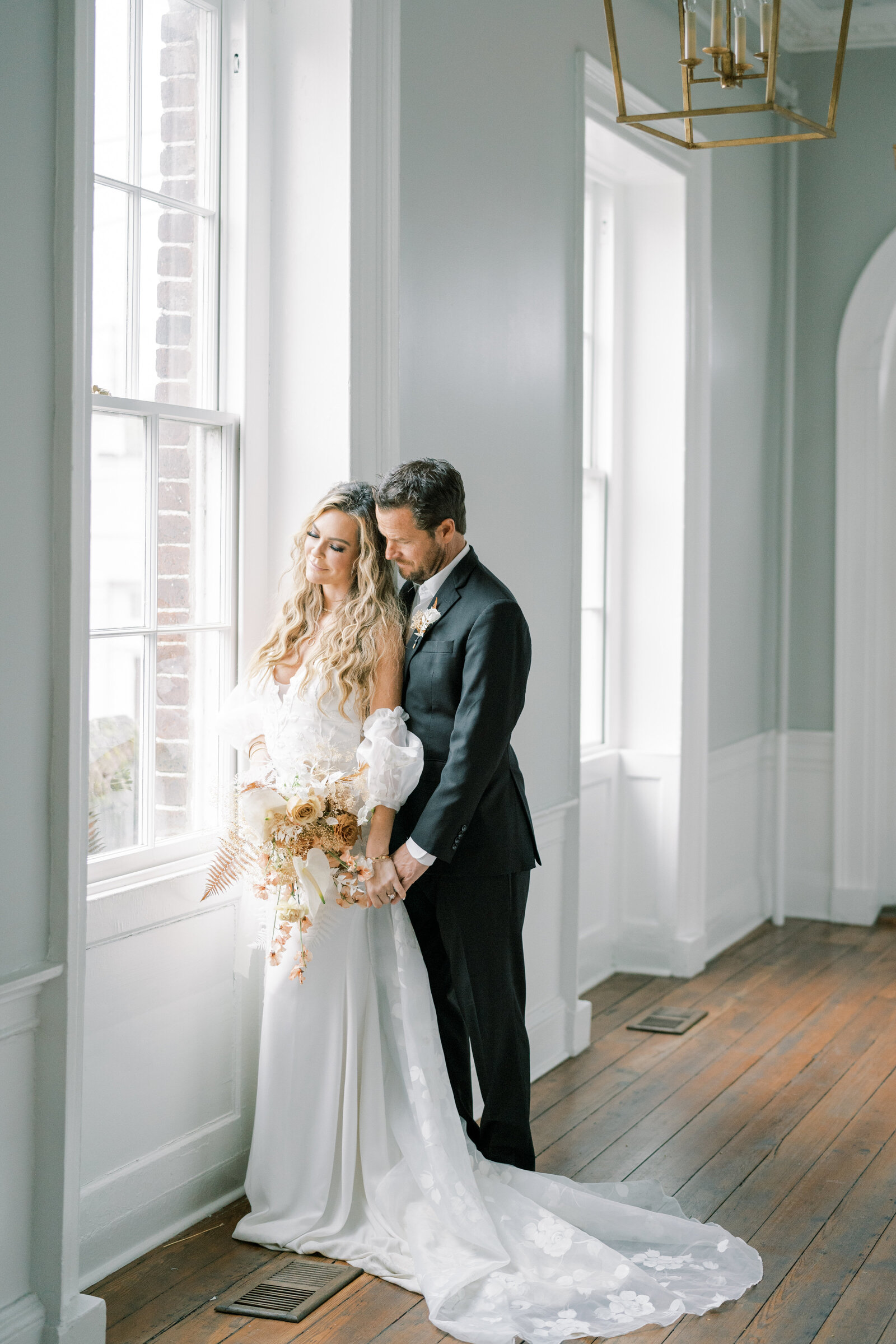 bride and groom standing at window  holding hands and looking outside at the gadsden house in charleston south carolina