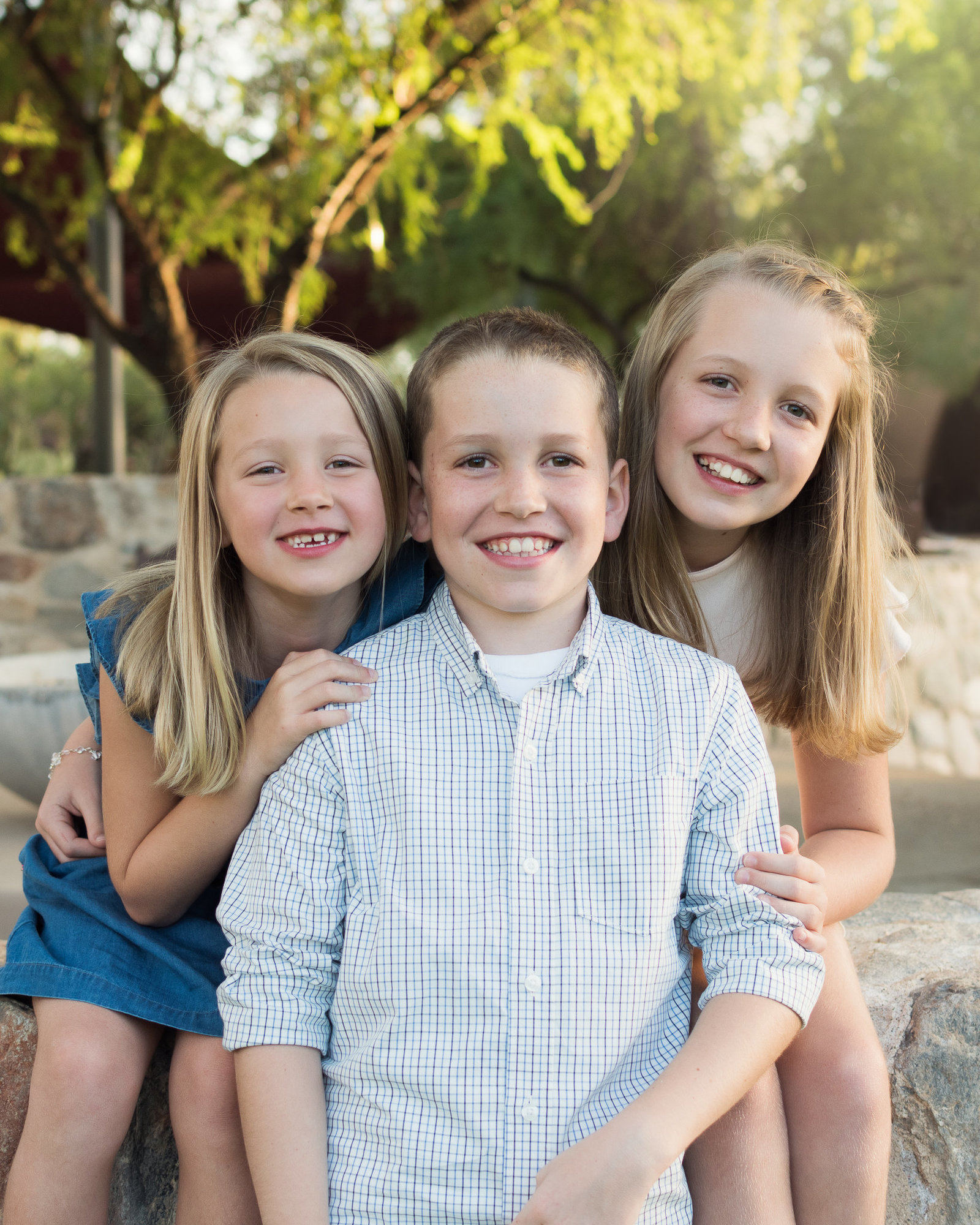 three children snuggling close to each other sitting on a stone wall