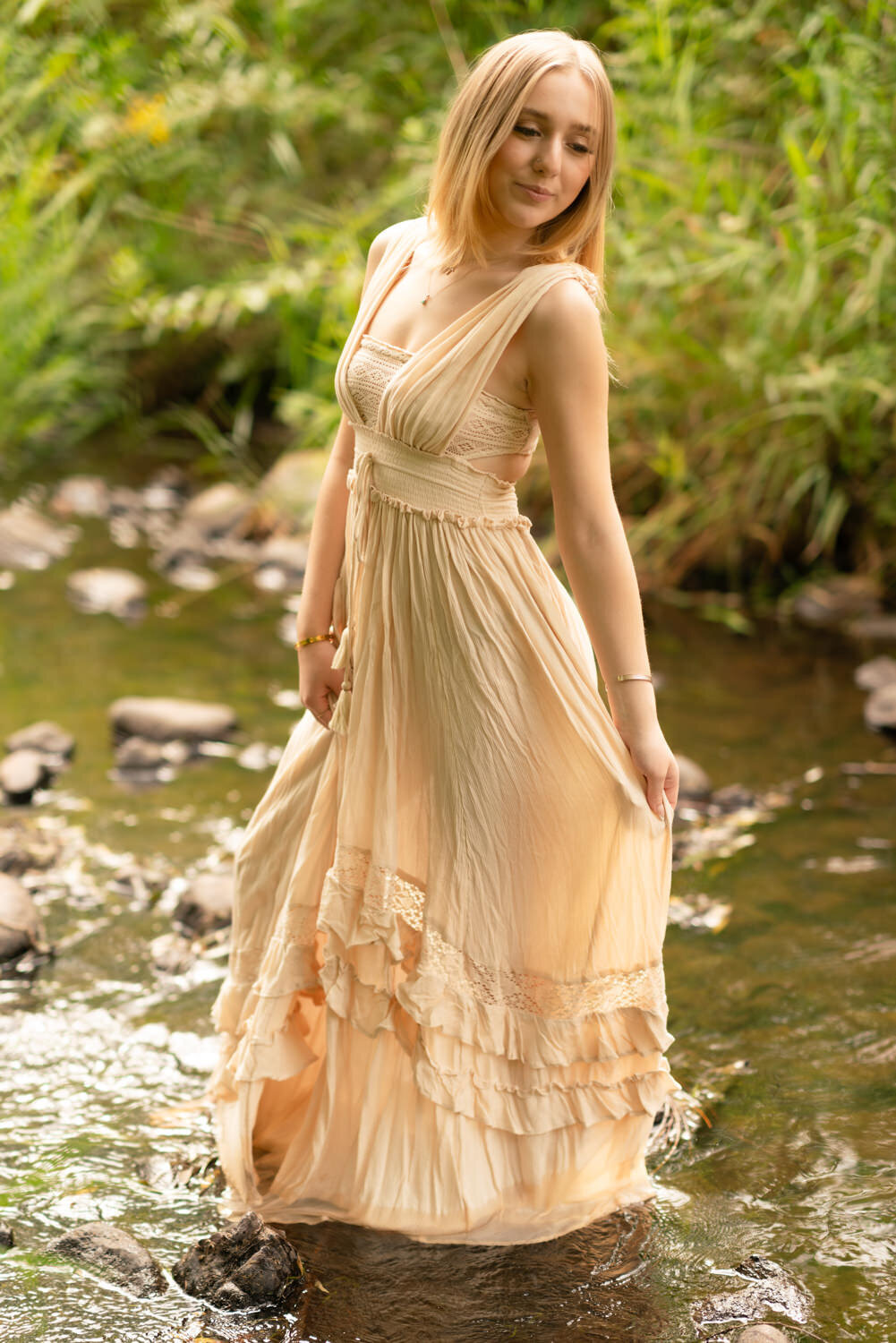 Senior girl walks through a creek in a long pink dress.