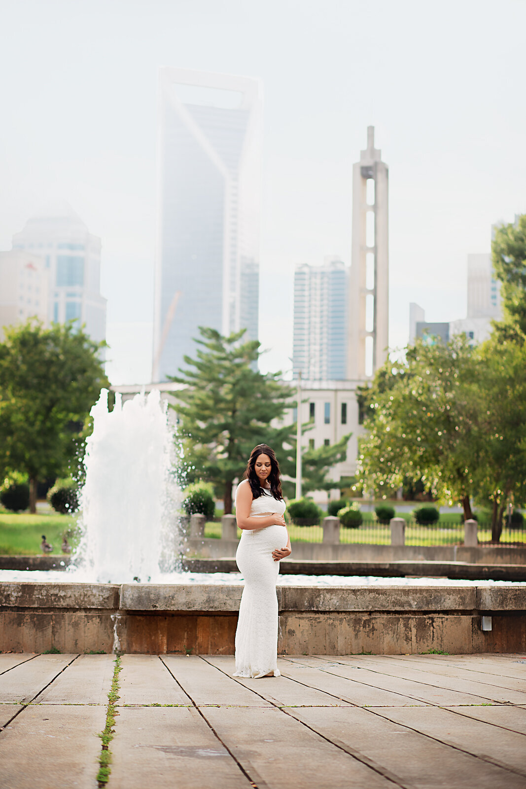 pregnant mom holding belly in front of fountain charlotte skyline