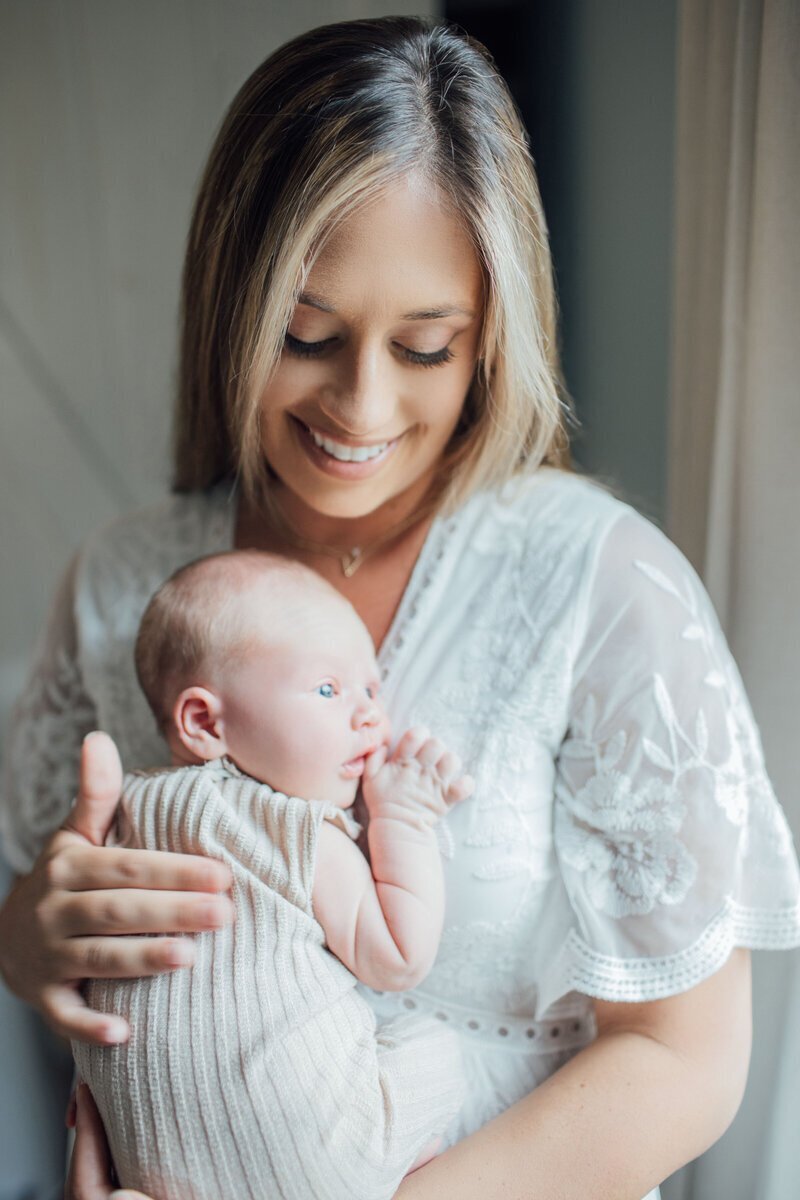 mom holding newborn baby by window, taken by new jersey newborn photographer
