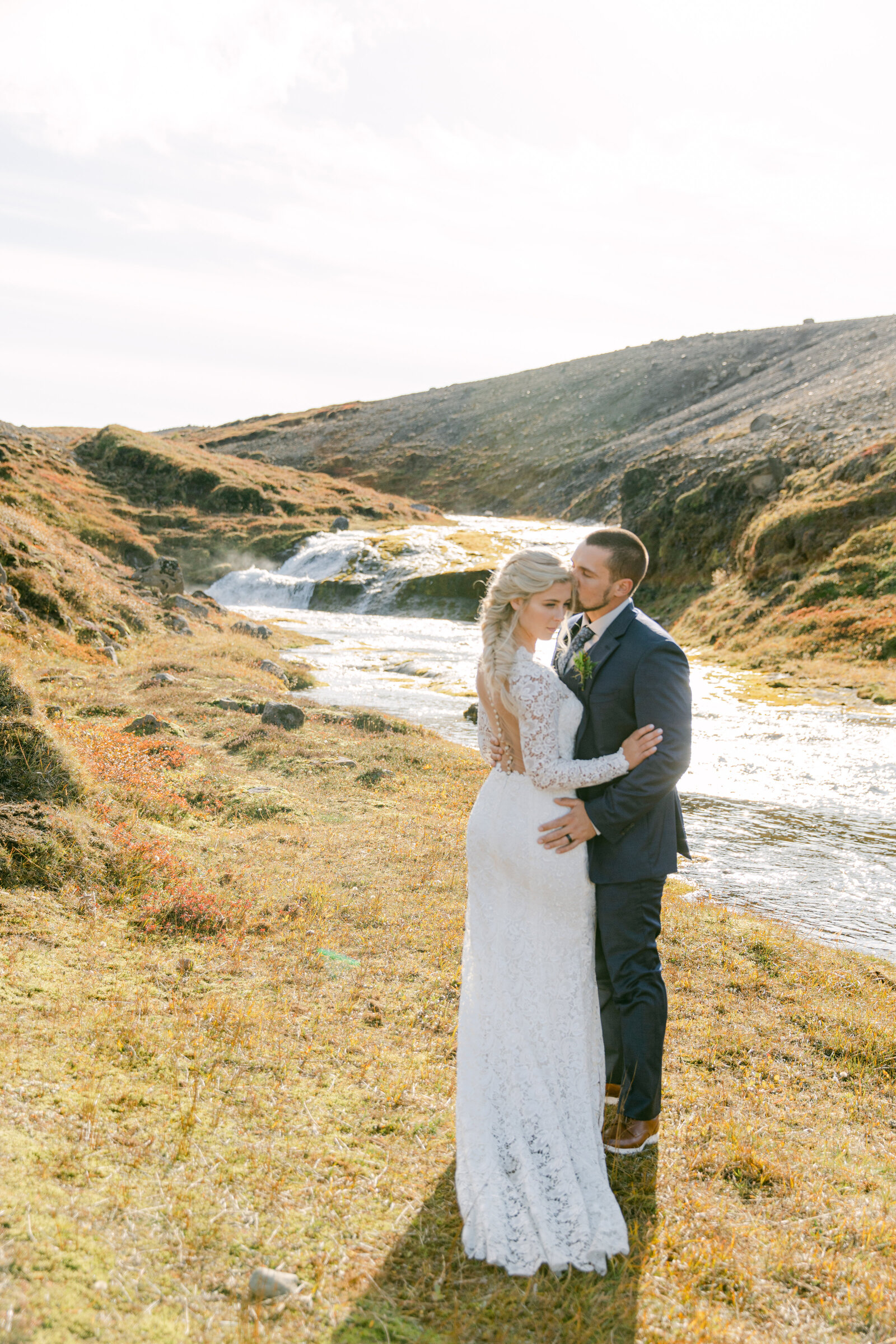 bride and groom face each other in iceland terrain near a waterfall