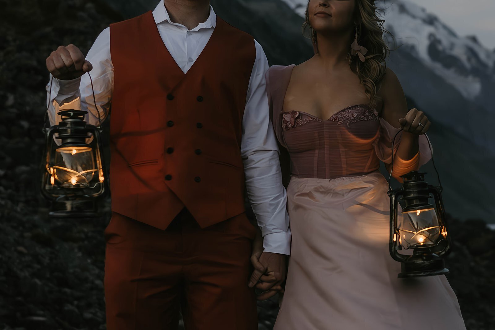 A couple holding lanterns embraces on rocky ground with mountains and a lake in the background at dusk, capturing the magic of a Utah desert photography retreat focused on real connection and growth.