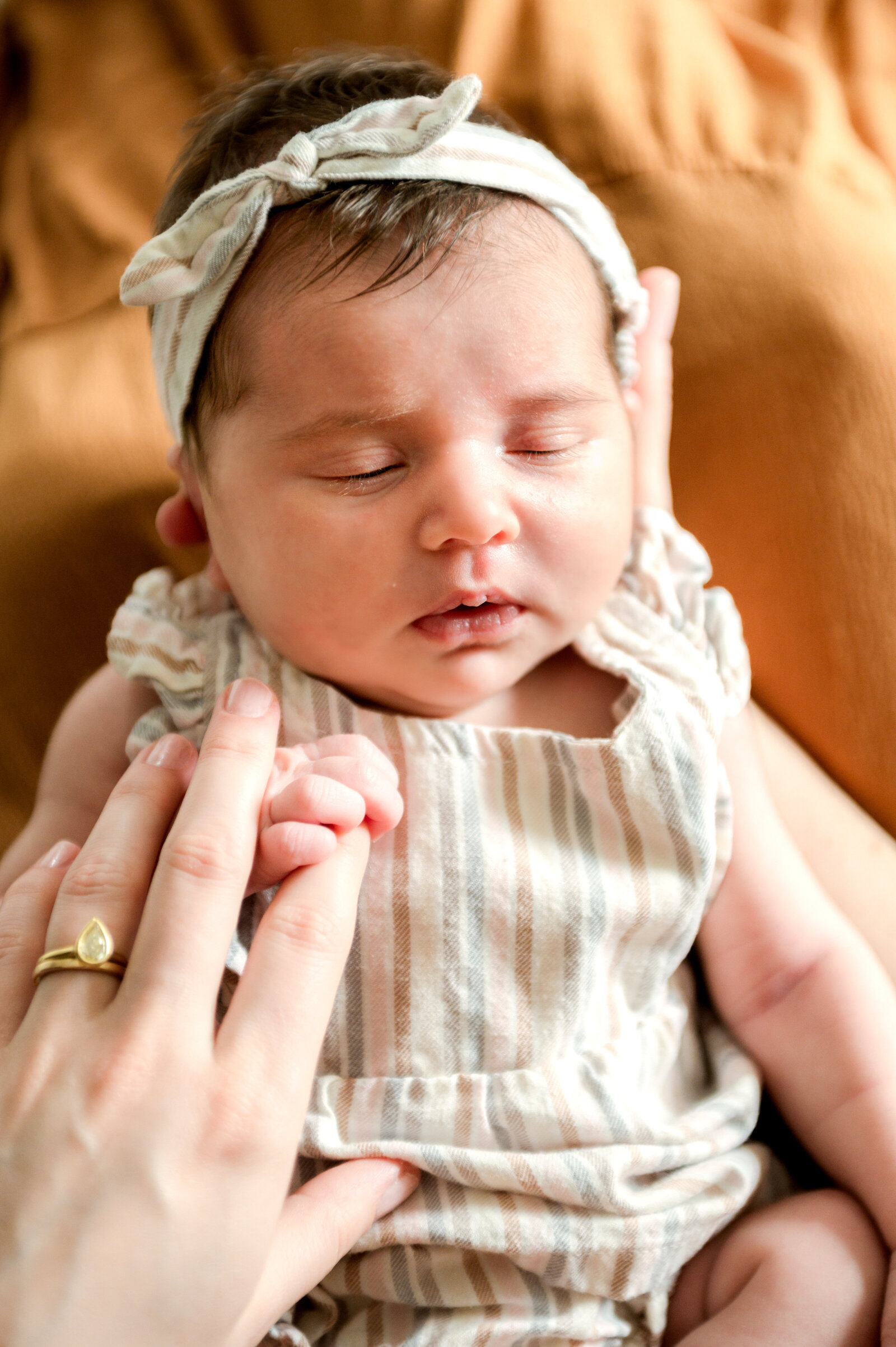 newborn girl with her finger around moms hand