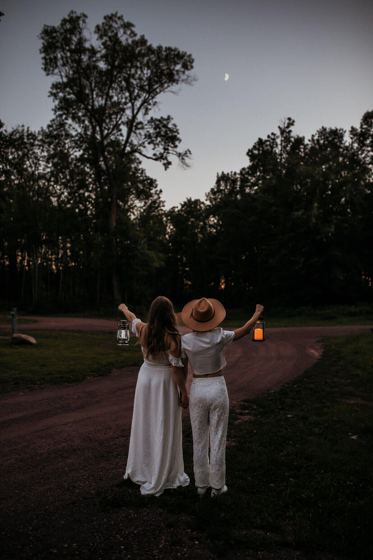 A couple holding hands and holding up lanterns at dusk
