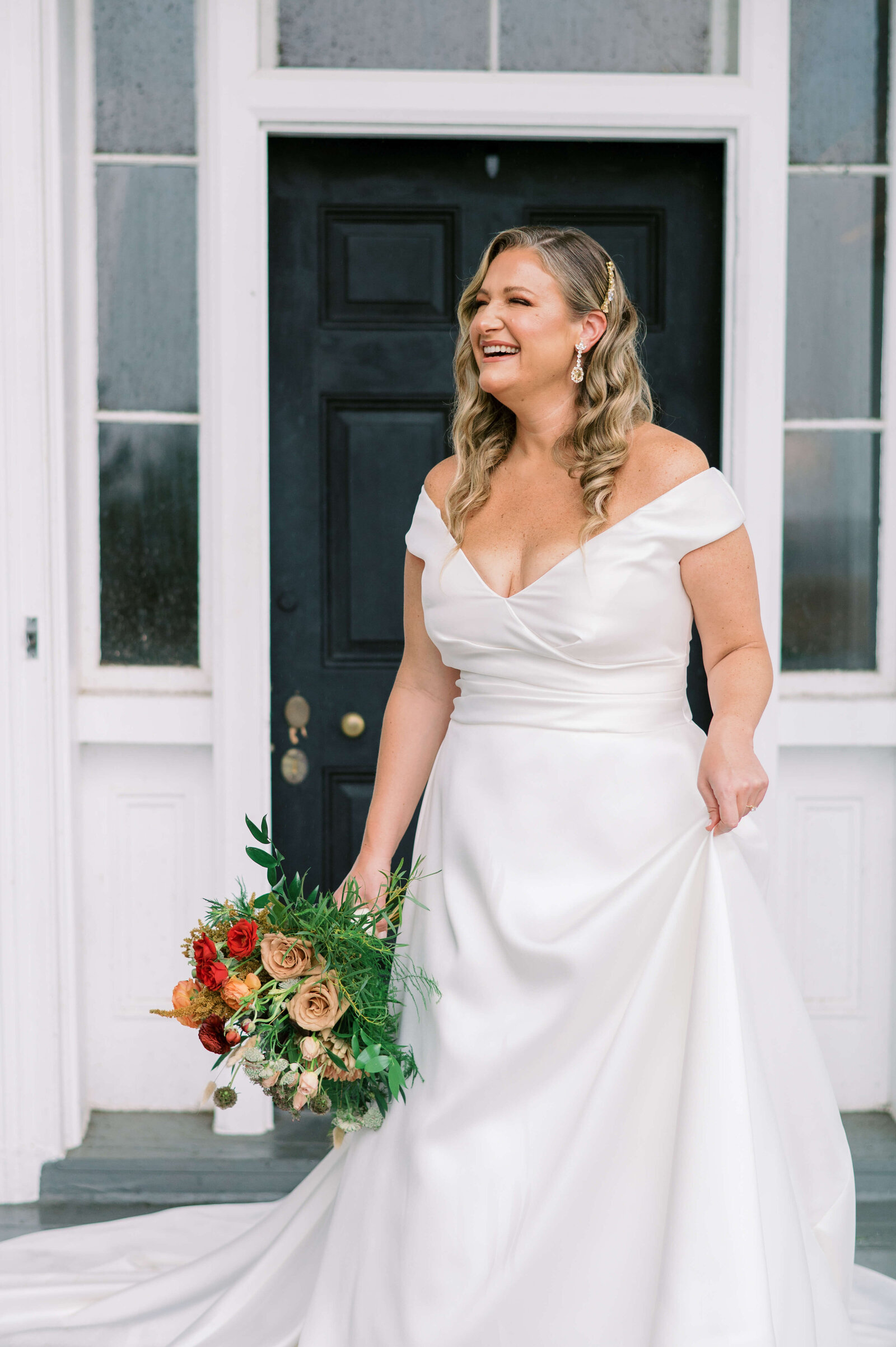Bride holds bouquet and dress skirt while laughing at the camera