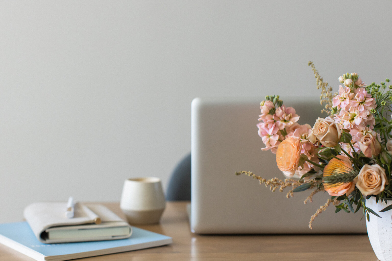 Colorful bouquet of flowers in a white vase on a wooden desk in front of a laptop.
