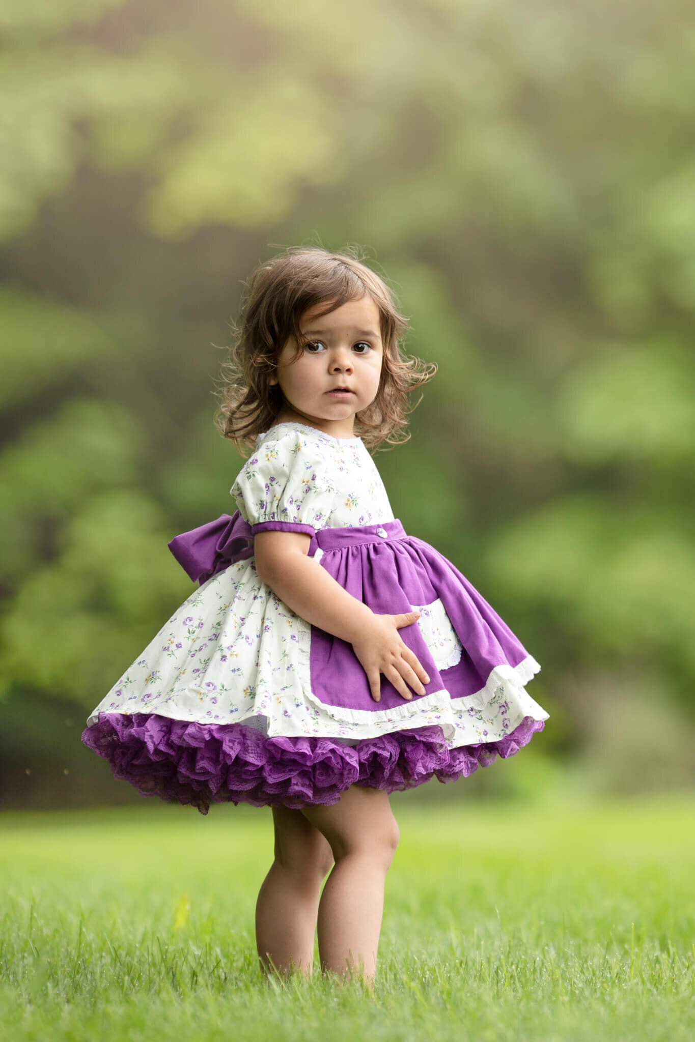 Toddler girl wearing vintage style purple floral dress standing in the grass