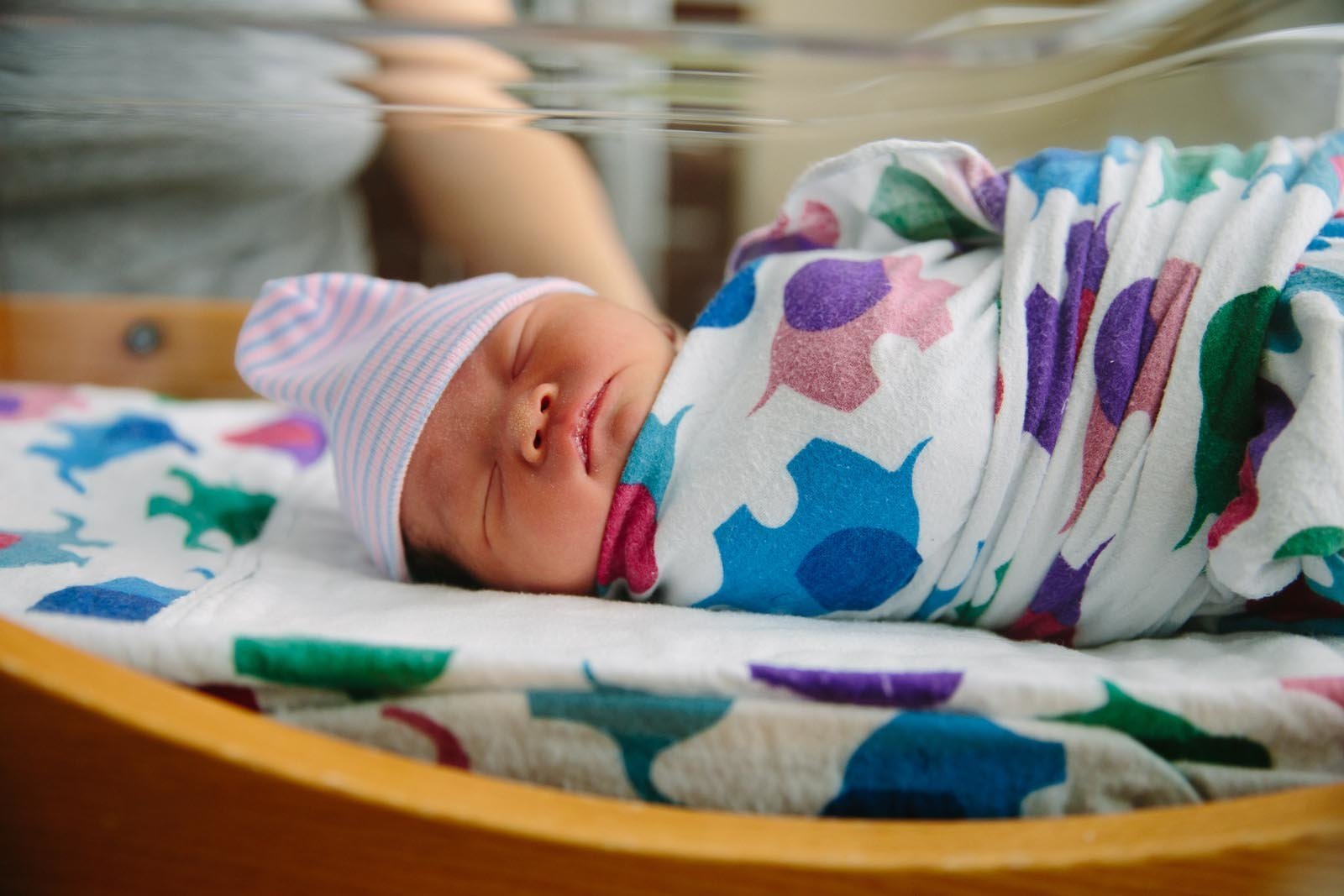 fresh 48 newborn photo of girl wrapped in hospital swaddle and knit hat sleeping in hospital bassinet