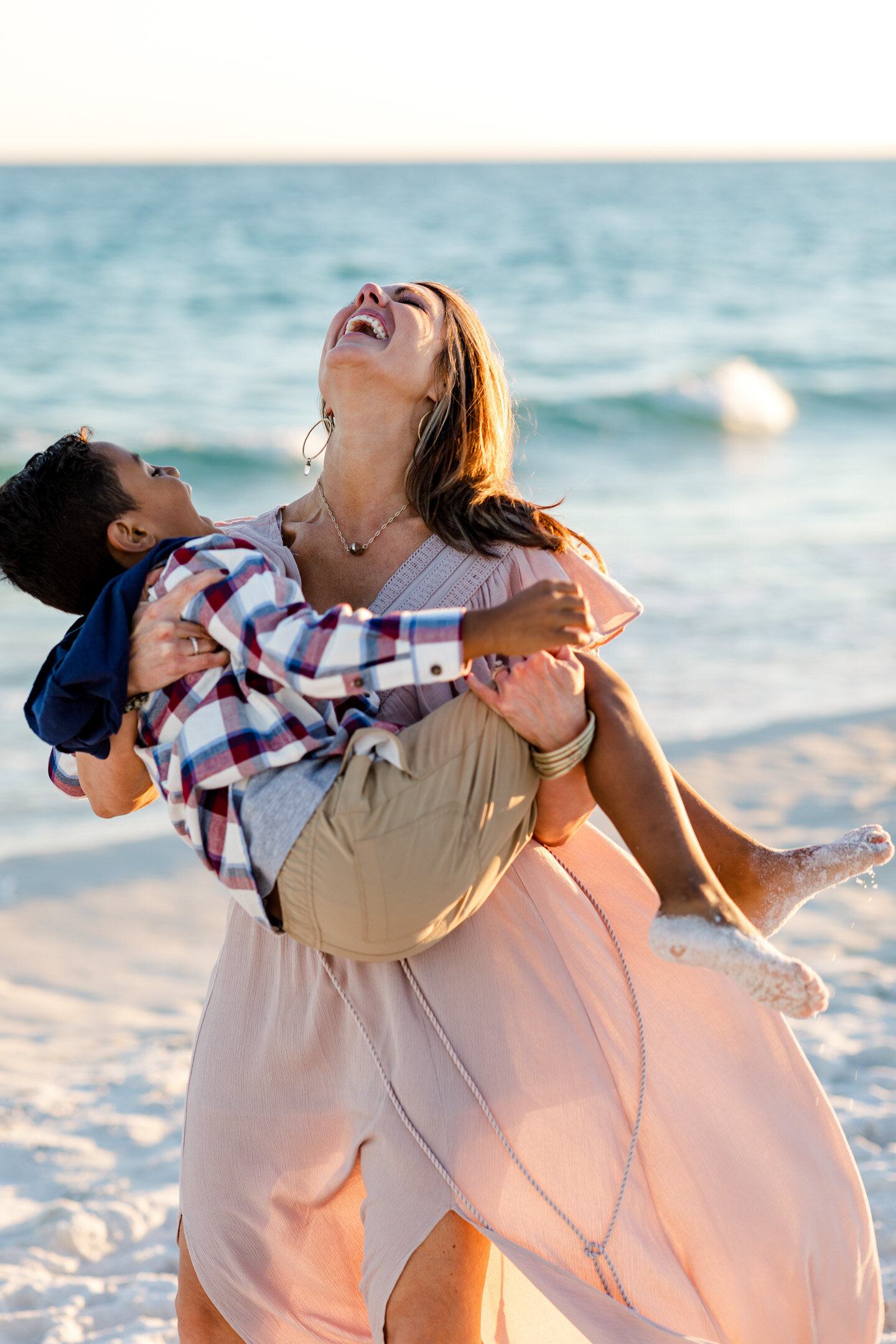 Mother laughing while holding son during family photo session at Pensacola Beach.
