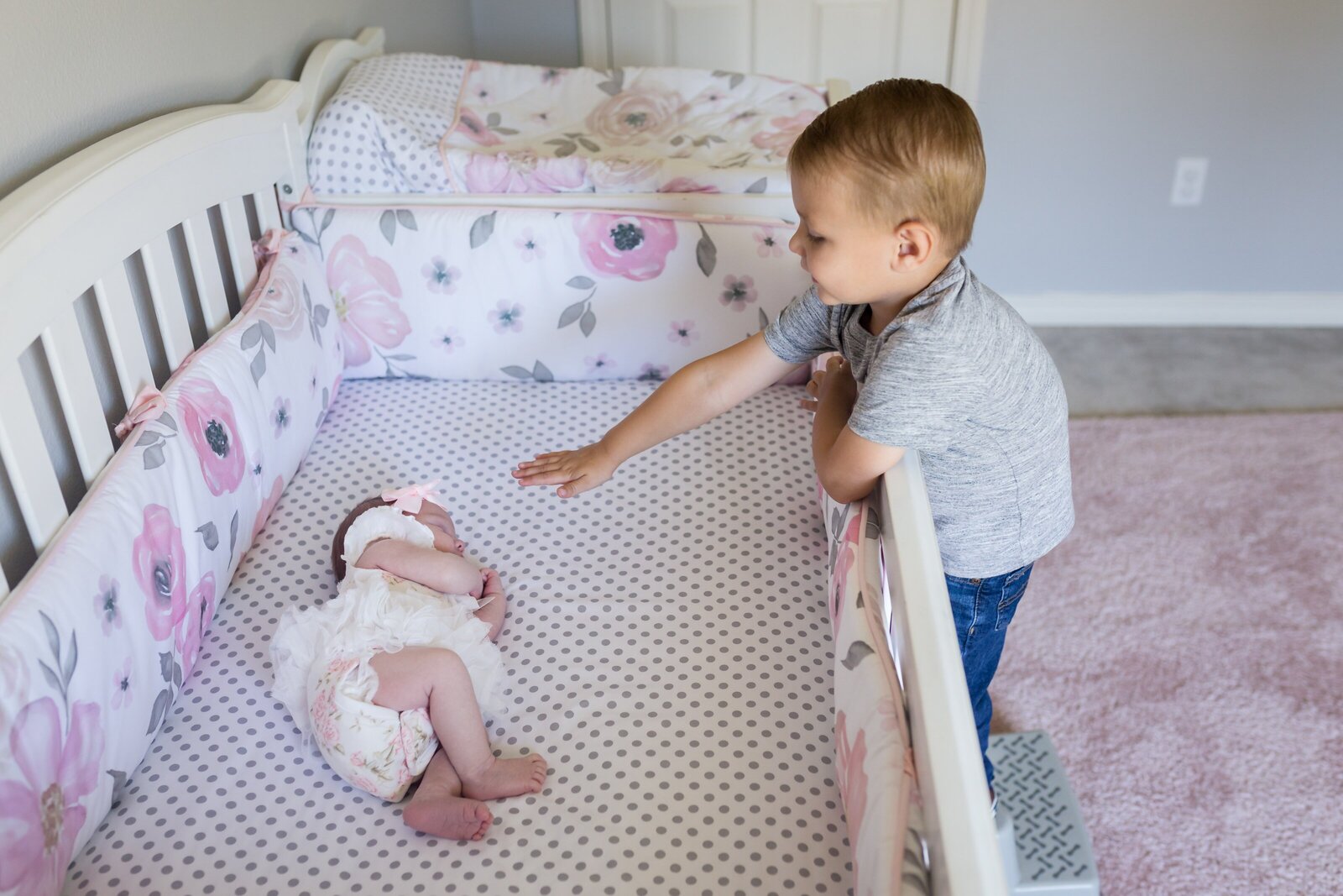 Big brother reaching for newborn sister in crib. In-home family photo session by Jennifer Beal photography.