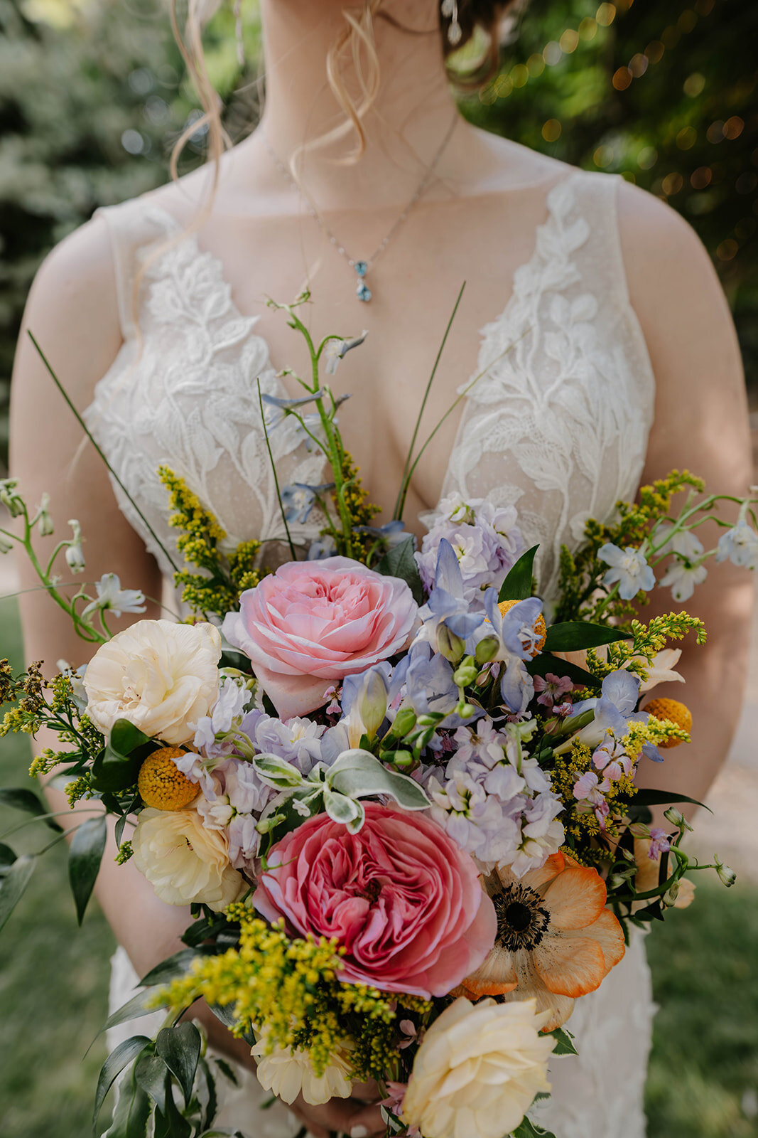 A bride in a lace dress holds a colorful bouquet of pink, yellow, and purple flowers—perfect for a Colorado wildflower elopement.