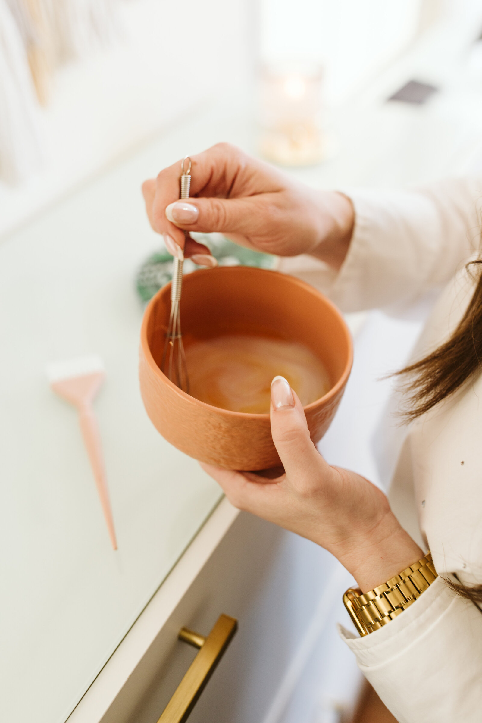 Close-up of a hair color mixture being stirred in a terracotta bowl by a stylist