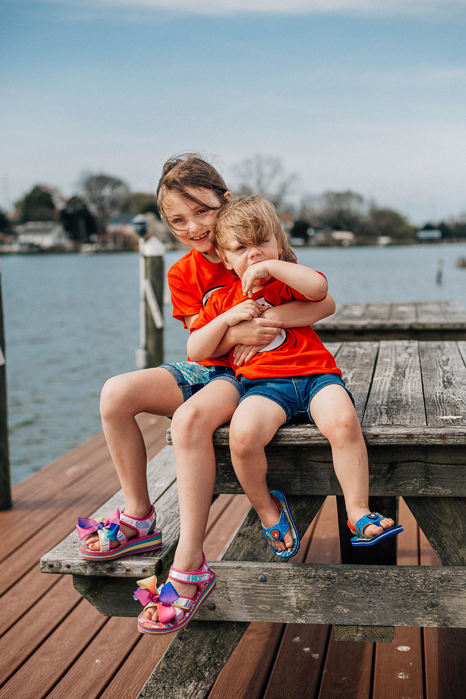 hampton roads photographers family photos with two children sitting on a picnic table on a dock in a lake hugging each other