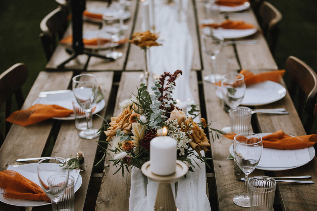 wood table with white plates, orange napkins and candles/florals