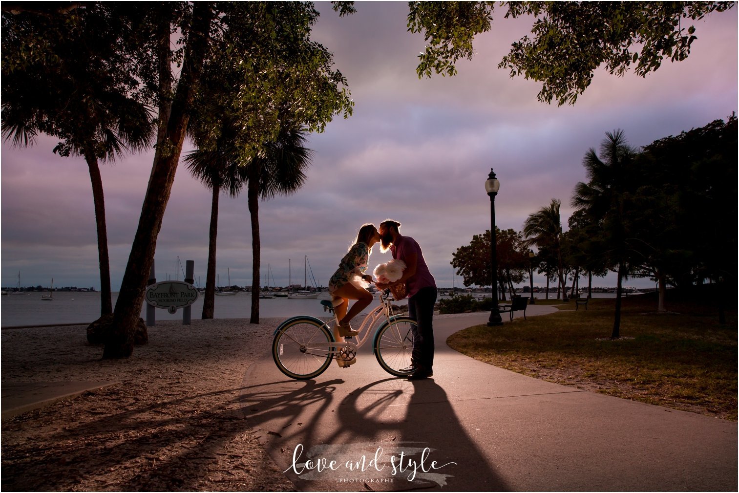 Sarasota Engagement Photography of couple kissing on a blue beach cruiser in Bayfront Park at sunset