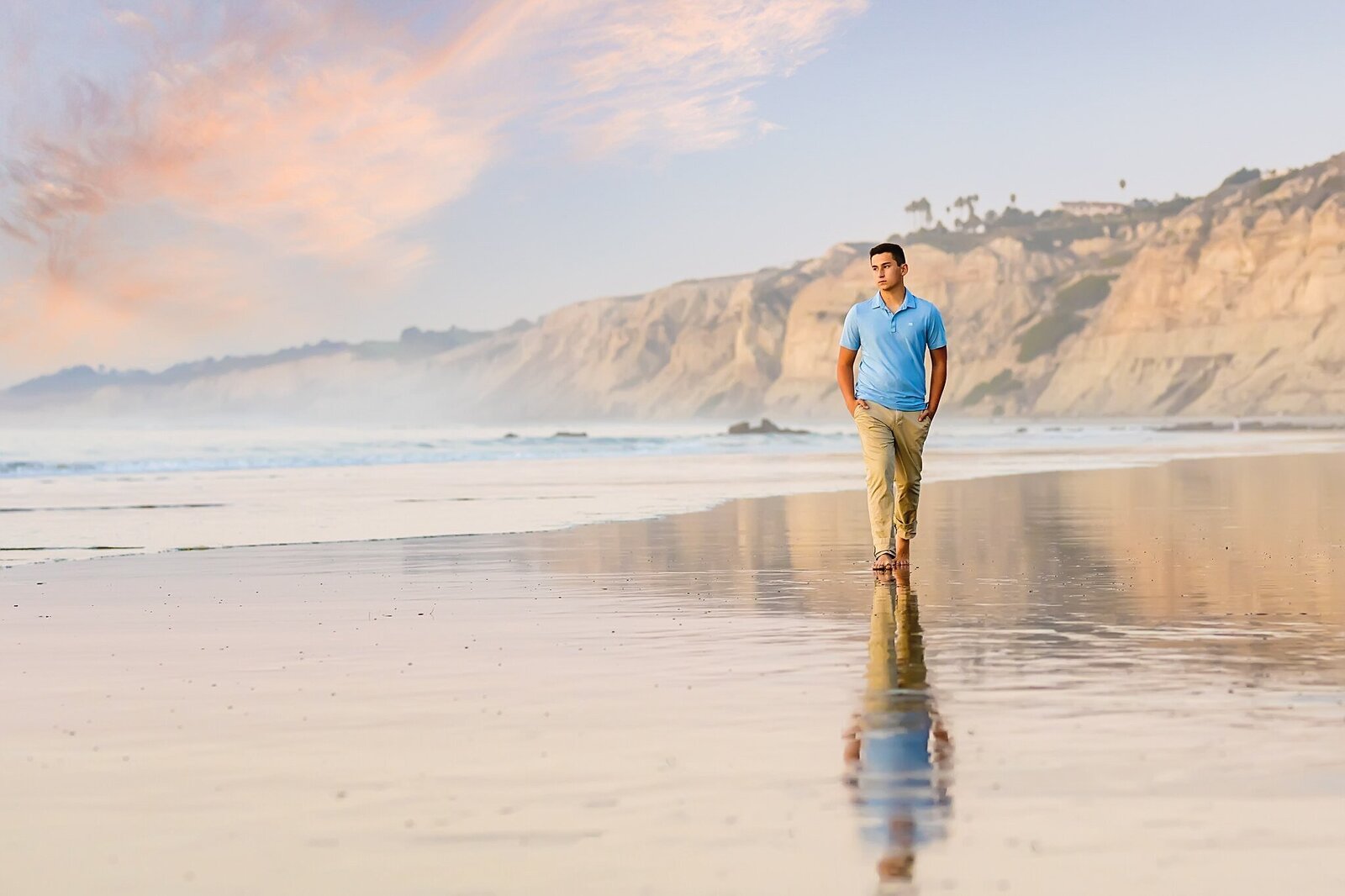 Senior boy walking along the beach in La Jolla with reflection showing on the wet sand