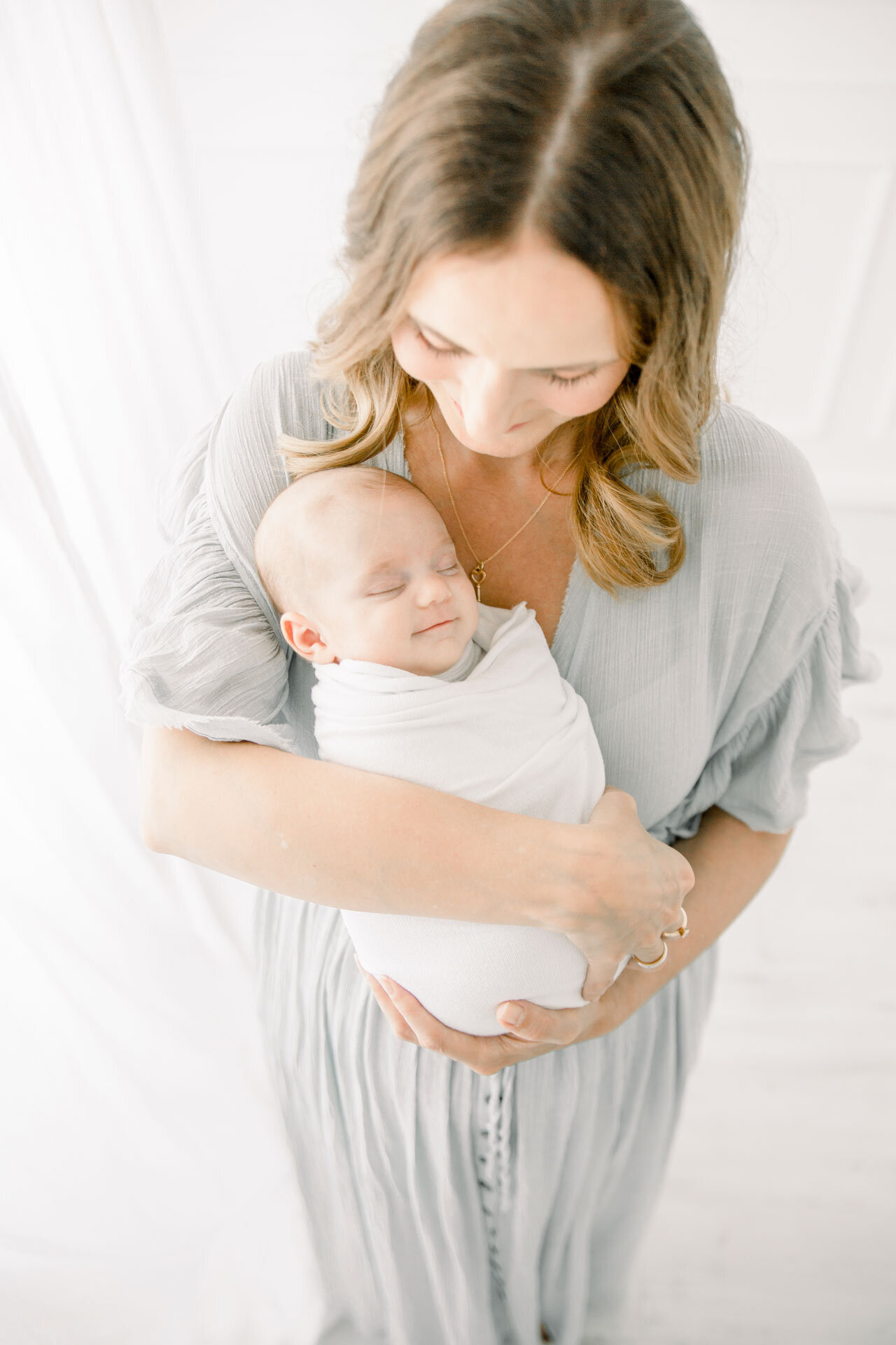 Neugeborenenshooting: Mama hält ihr Neugeborenes im Arm, das beim Schlafen lächelt.