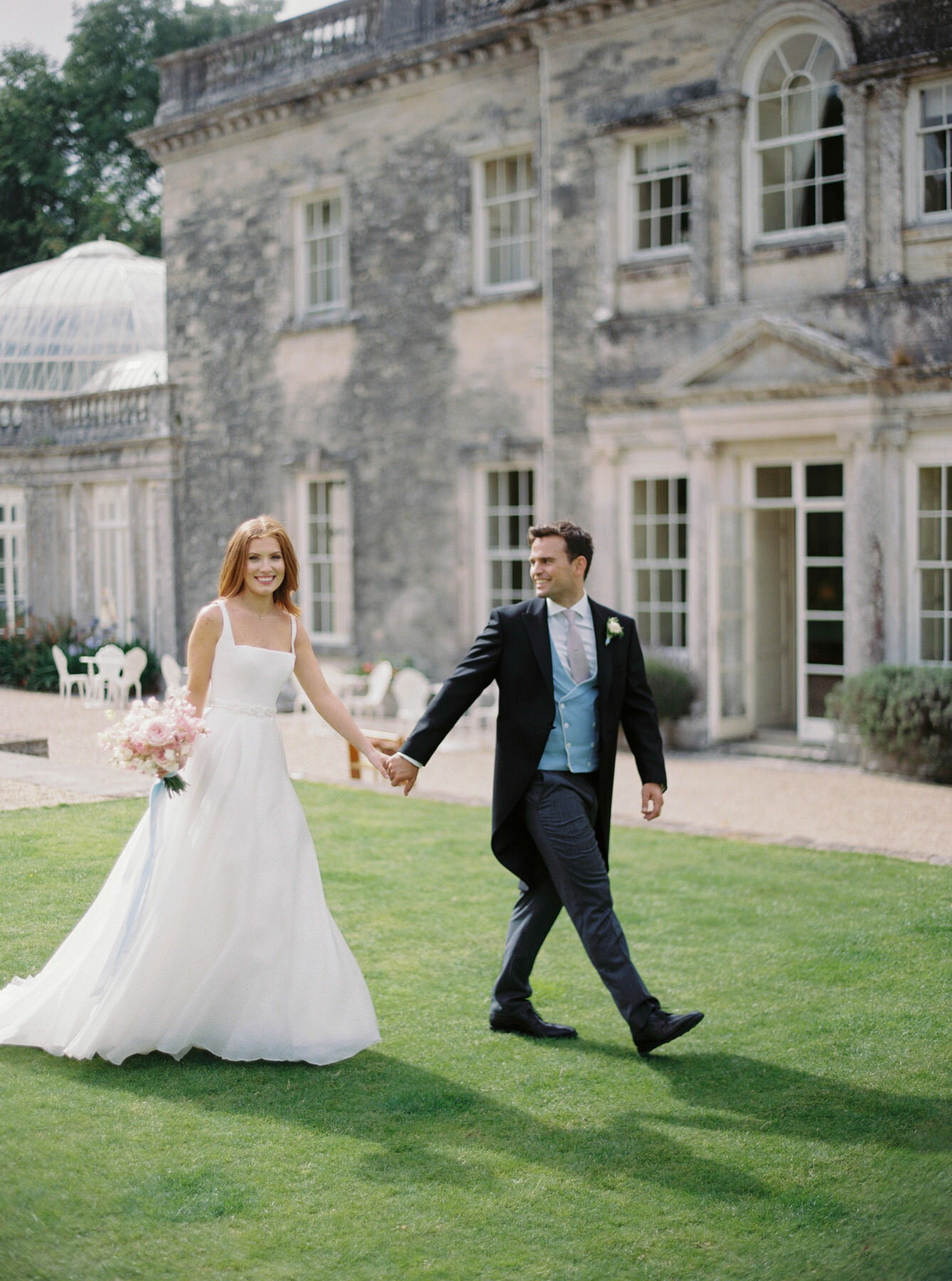 Bride and groom holding hands while walking in front of came house estate