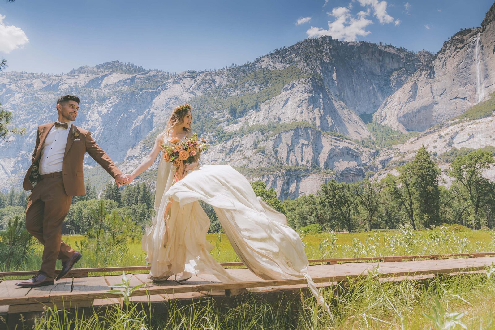A groom leads his bride by hand as her dress flows in the breeze in Yosemite National Park.