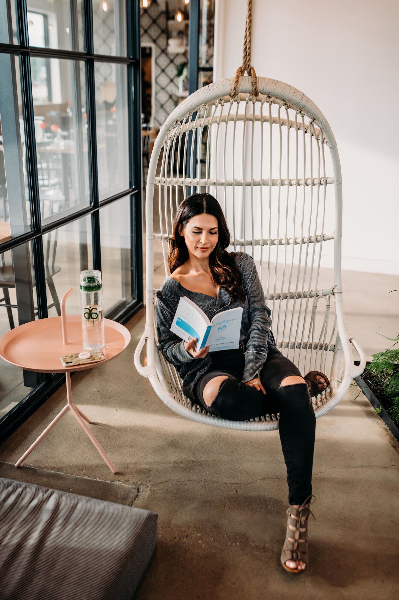 Branding Photographer, a woman sits in a boho style wicker chair swing reading a book