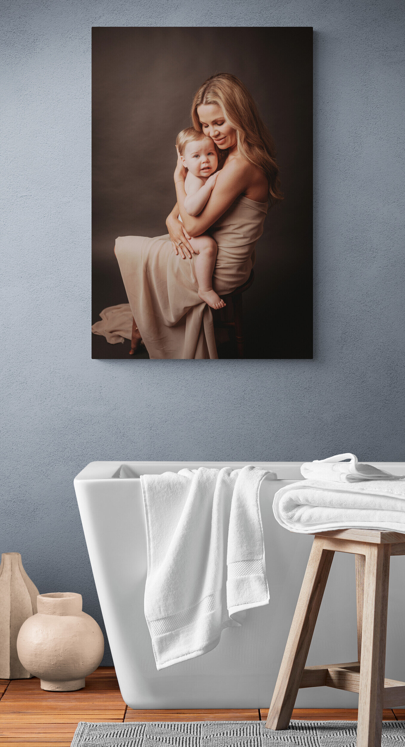 Large photographic artwork hanging on master bathroom wall above stand alone tub of mom and baby holding each other