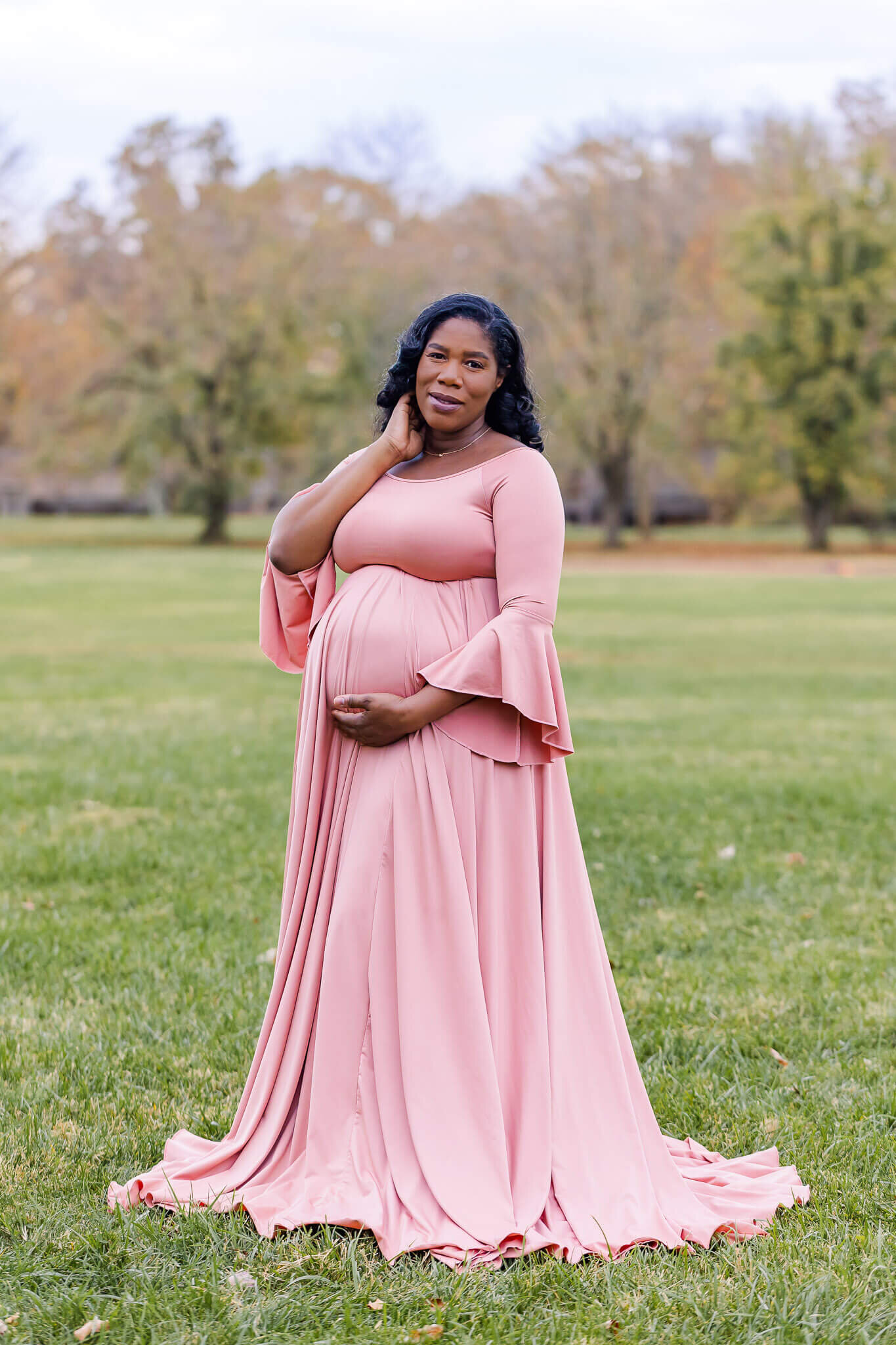 An expecting mother wearing a pink dress posing for her maternity portraits at Fort Hunt.