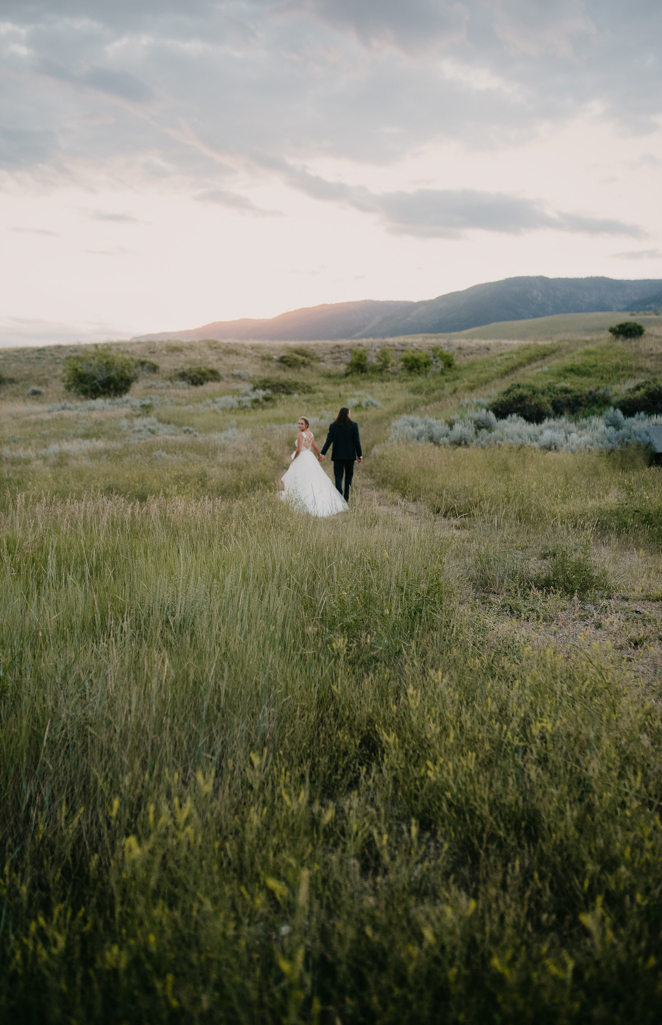 Gorgeous photo of newlyweds walking through the ranch field, bride is looking back in Casper Wyoming.