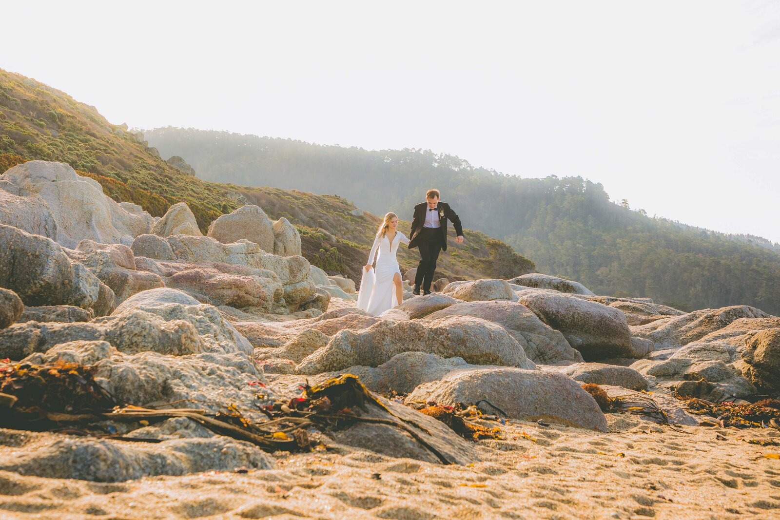 A bride and groom go on an adventure over large rocks during their beach elopement.