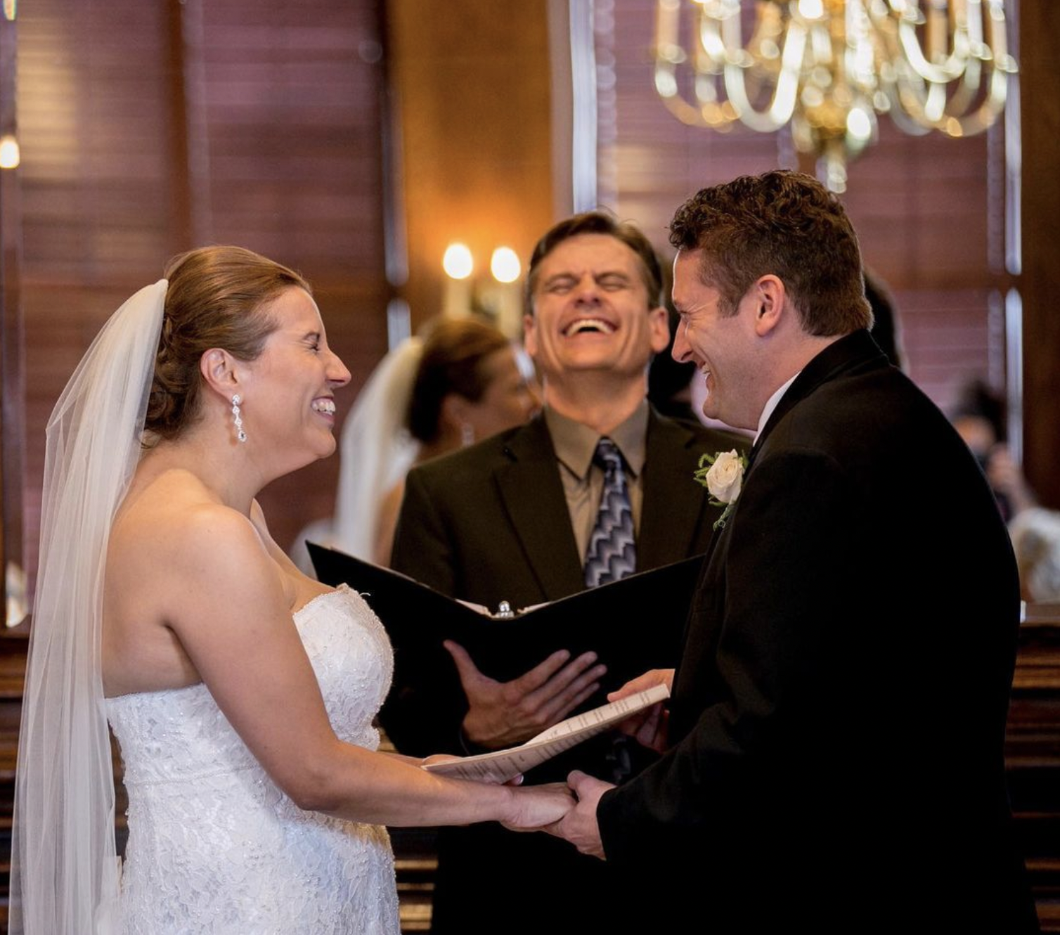 Bride, groom, and officiant laugh during wedding ceremony