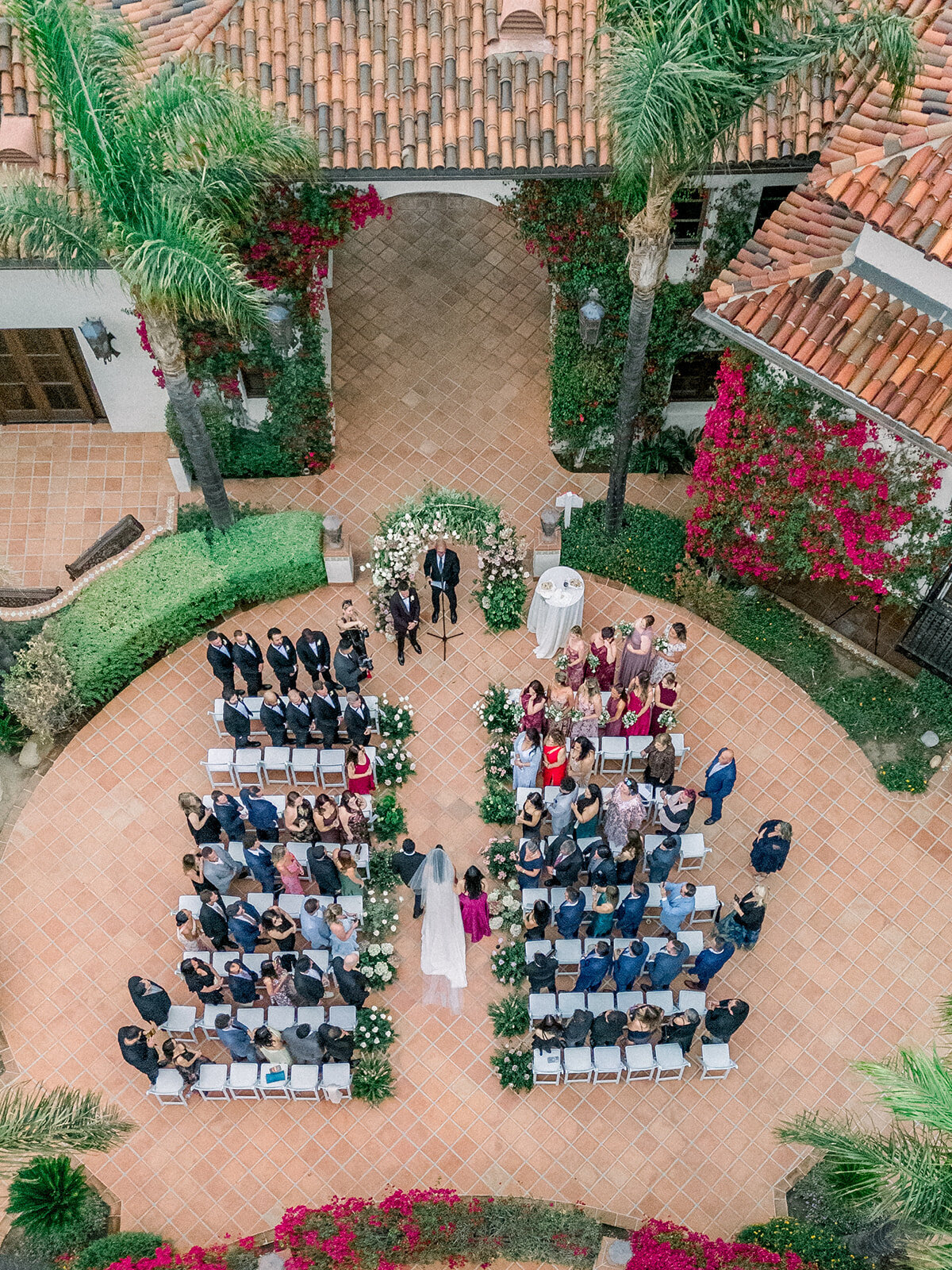 Aerial documentary-style photo of wedding ceremony setup at Hummingbird Nest Ranch with lush gardens and terracotta architecture.